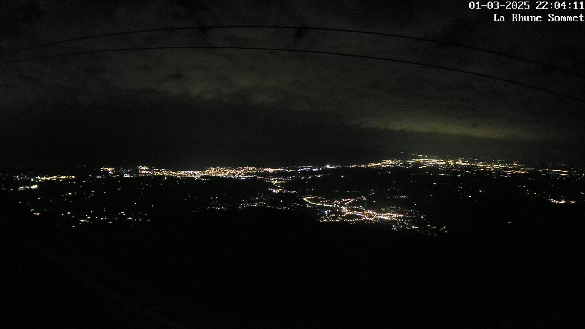 A nighttime, high-angle view shows a sprawling city illuminated with scattered lights under a dark, cloudy sky.