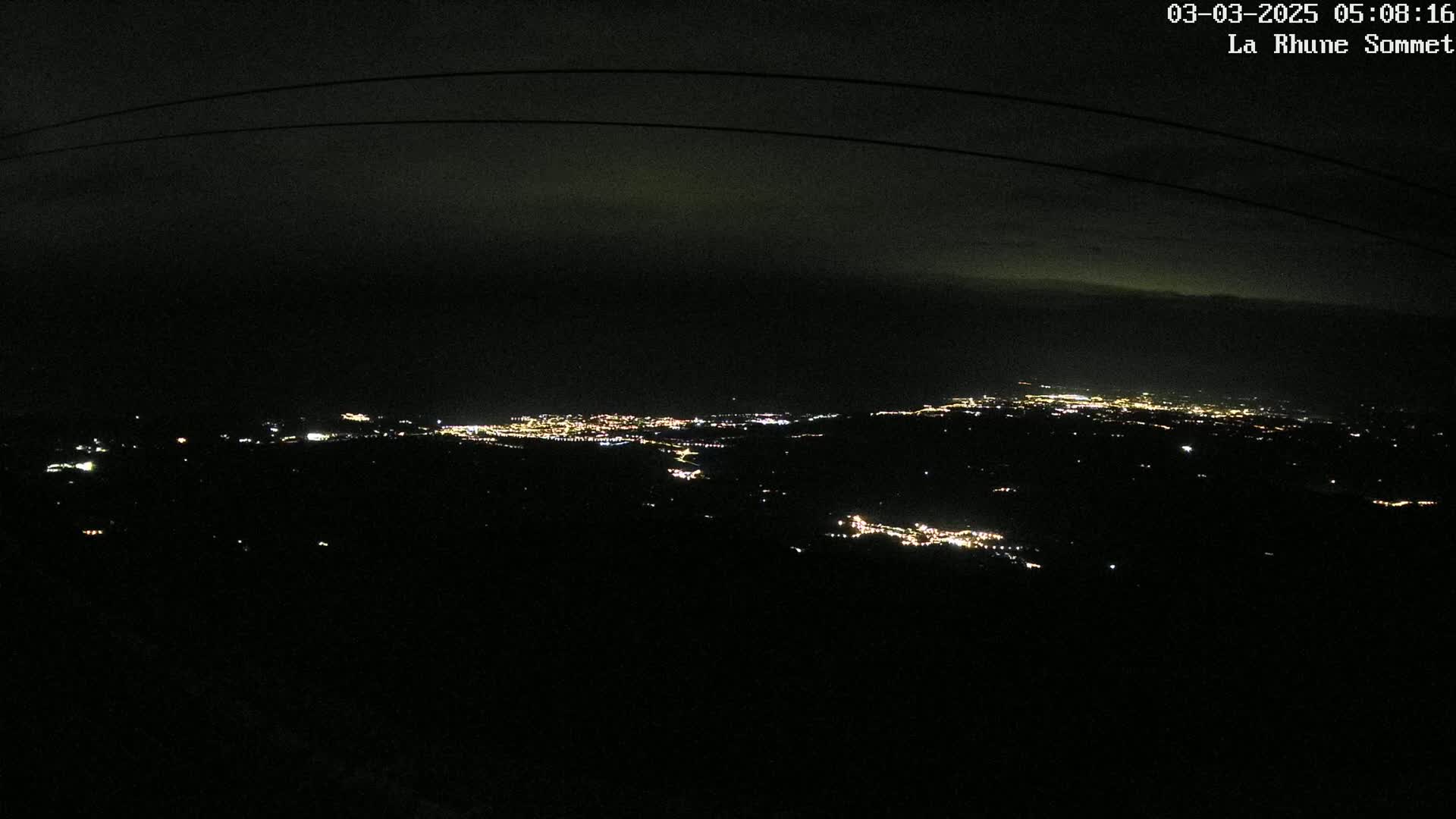 A nighttime, high-angle view shows a sprawling city illuminated by scattered lights below a dark, mostly clear sky.