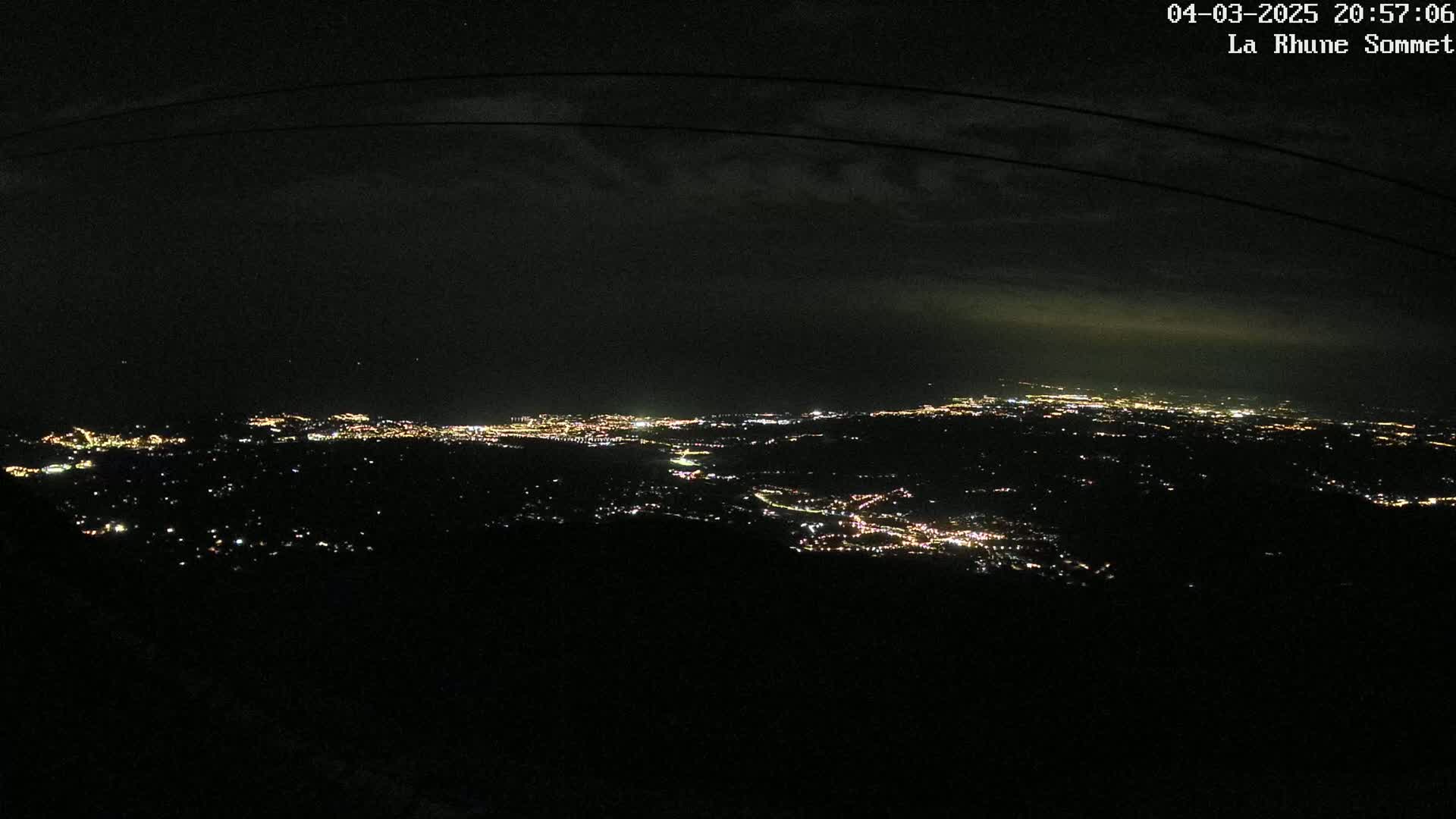 A nighttime view from a high vantage point shows a sprawling city illuminated by scattered lights under a dark, cloudy sky.