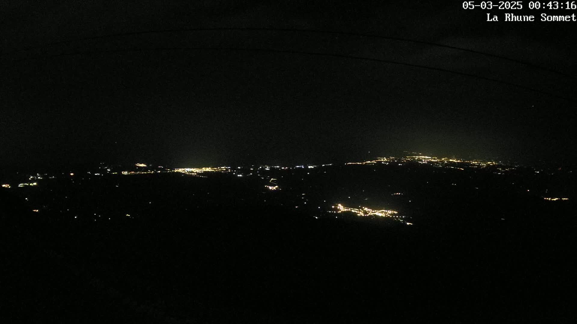 A nighttime view from a high vantage point shows a distant city's lights scattered across a dark landscape under a clear, dark sky.