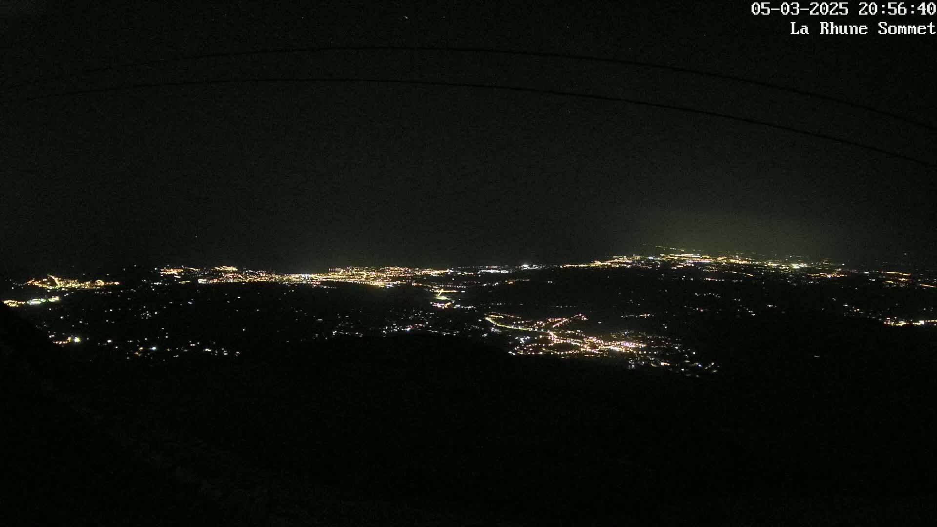 A nighttime, high-angle view shows a sprawling city illuminated by many small lights, extending across a dark landscape under a clear, starlit sky.