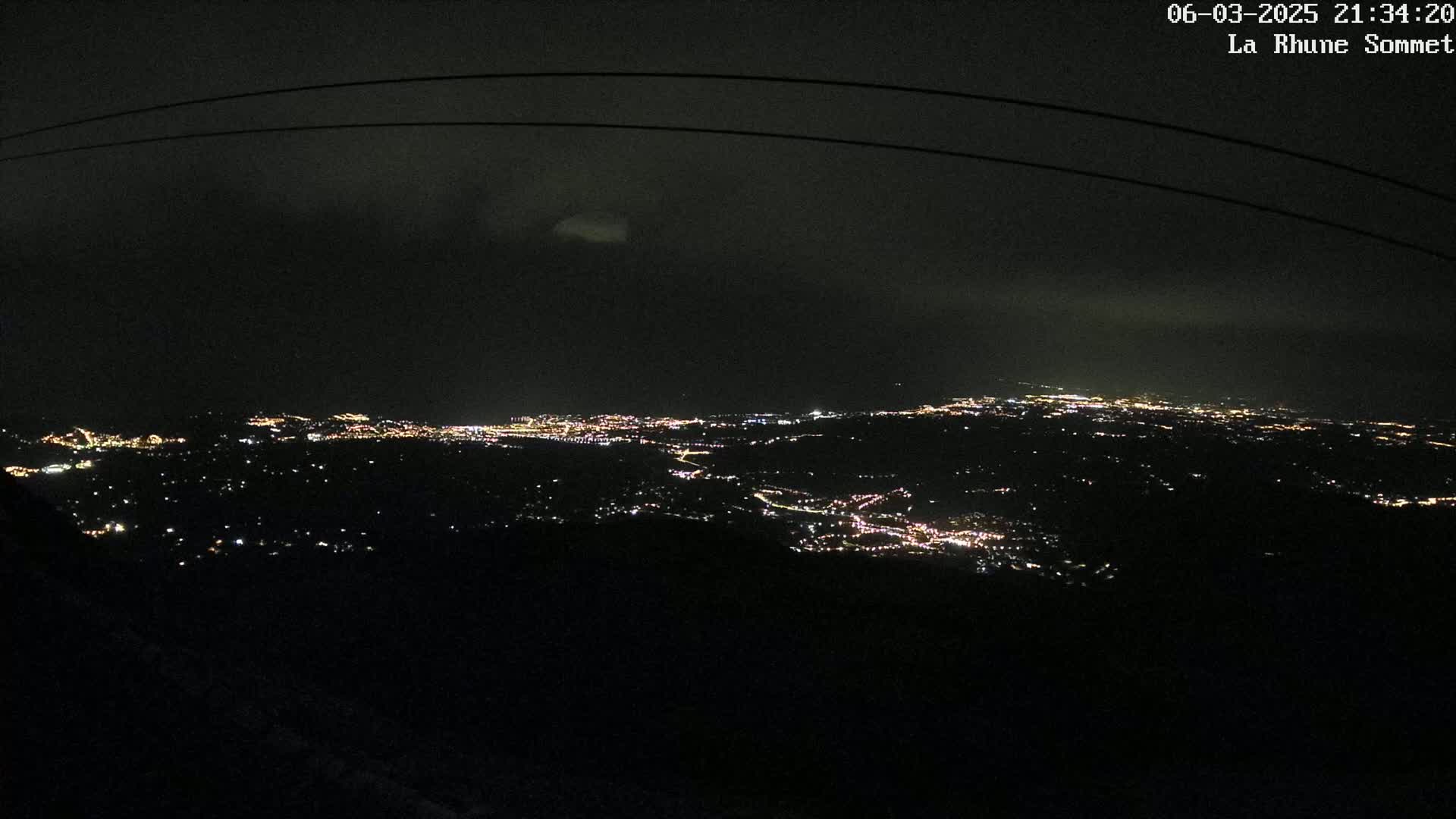 A nighttime, high-angle view of a city's lights spread across a dark landscape under a mostly clear sky.