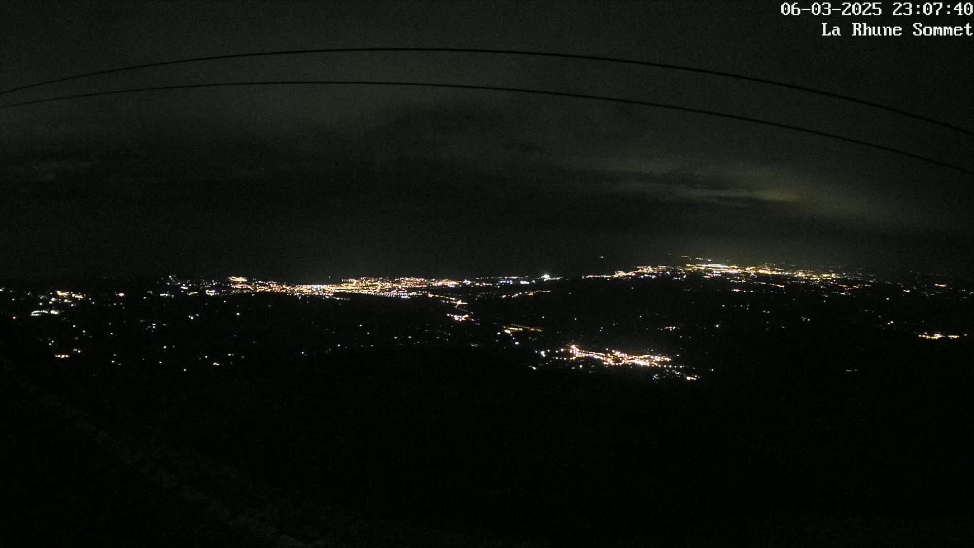 A nighttime, high-angle view shows a distant city glowing with lights under a dark, cloudy sky.