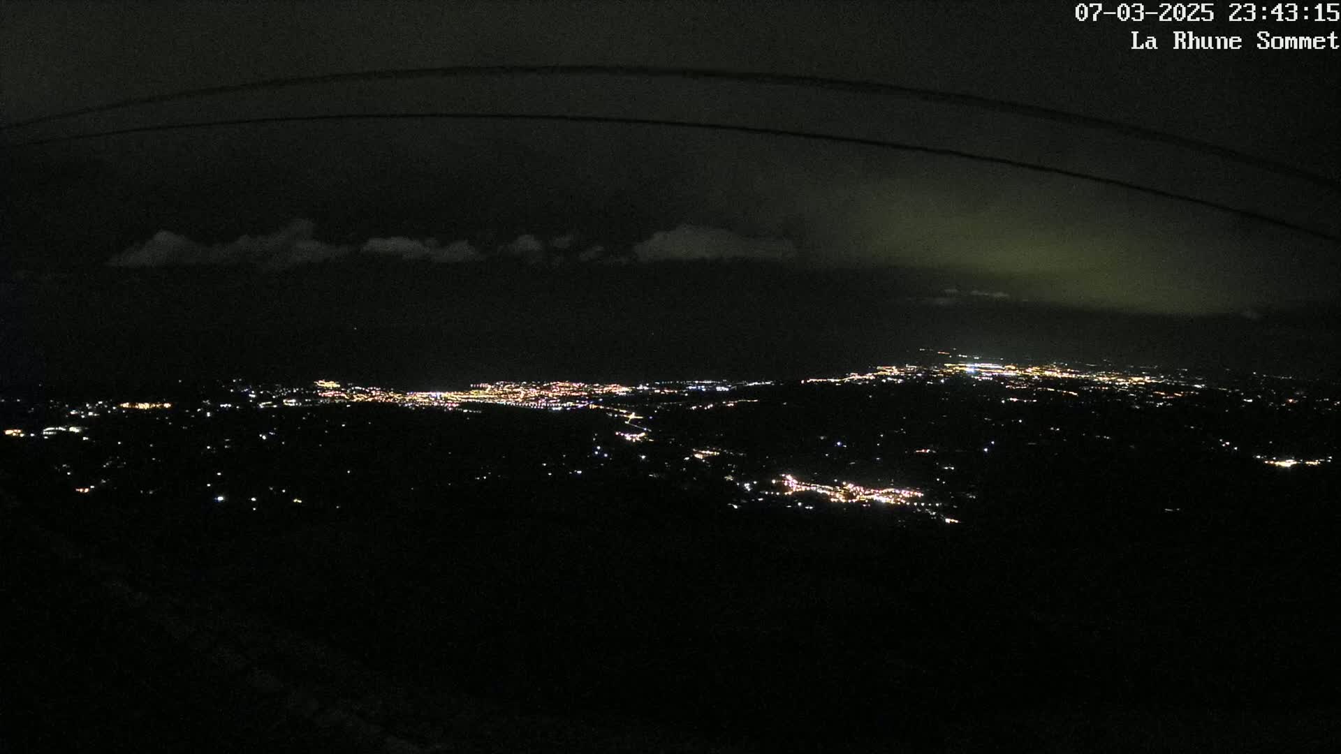 A nighttime, high-angle view shows a sprawling city illuminated below a partly cloudy sky.
