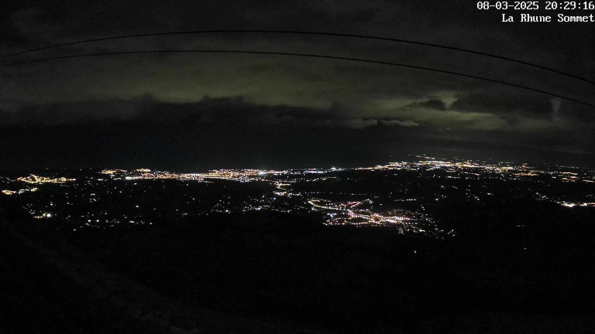 A nighttime view shows a sprawling city illuminated below, under a dark, cloudy sky.