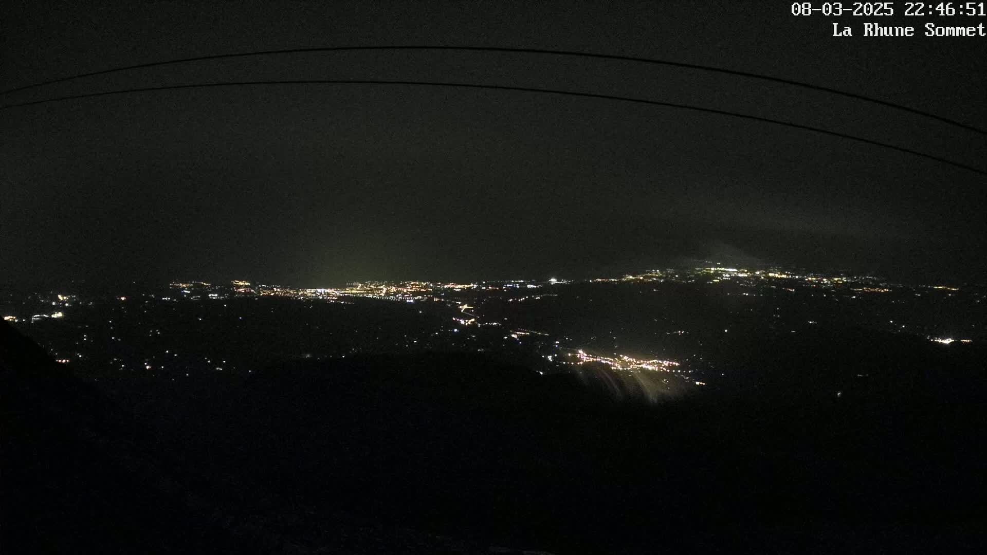 A nighttime view from a high vantage point shows a sprawling city illuminated with faint lights under a dark, possibly cloudy sky.