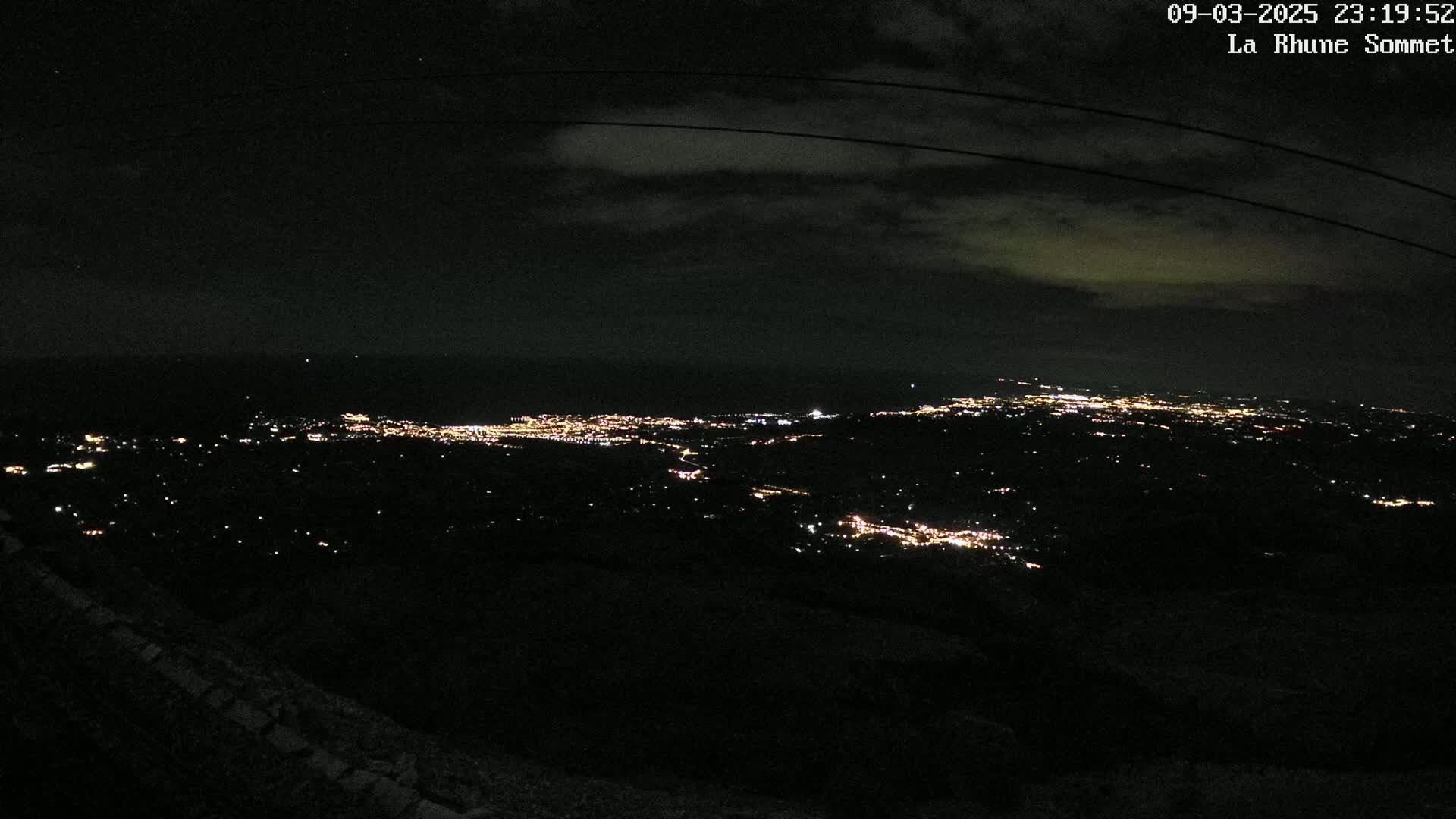 A nighttime, high-angle view shows a sprawling city illuminated with scattered lights under a partly cloudy sky.