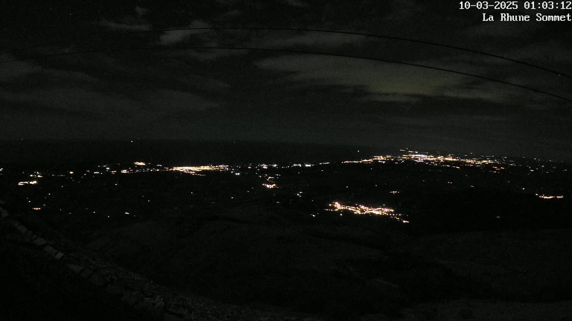 A nighttime, high-angle view of a distant city's lights spread across a dark landscape under a mostly clear sky.
