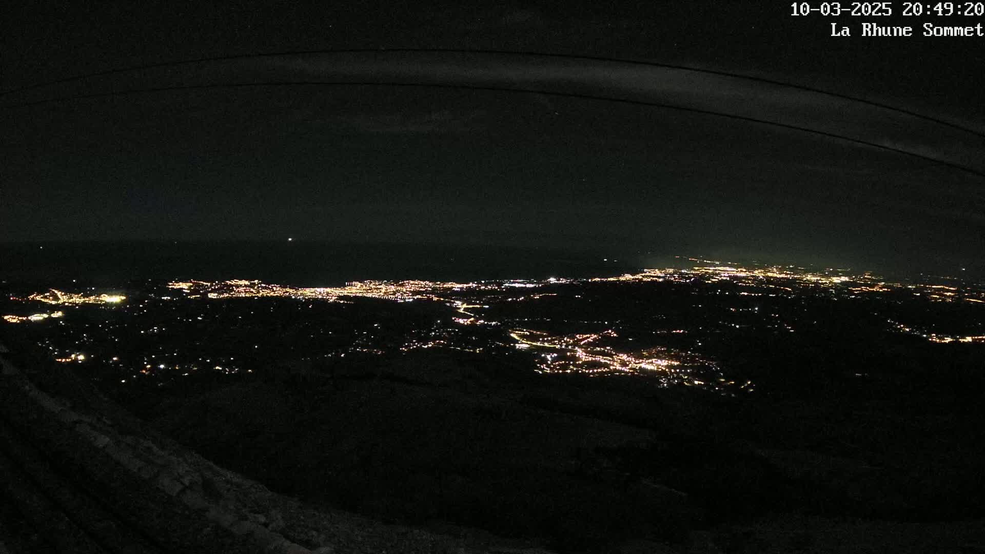 A nighttime view from a high vantage point shows a sprawling city illuminated by countless lights below, under a dark, clear sky.