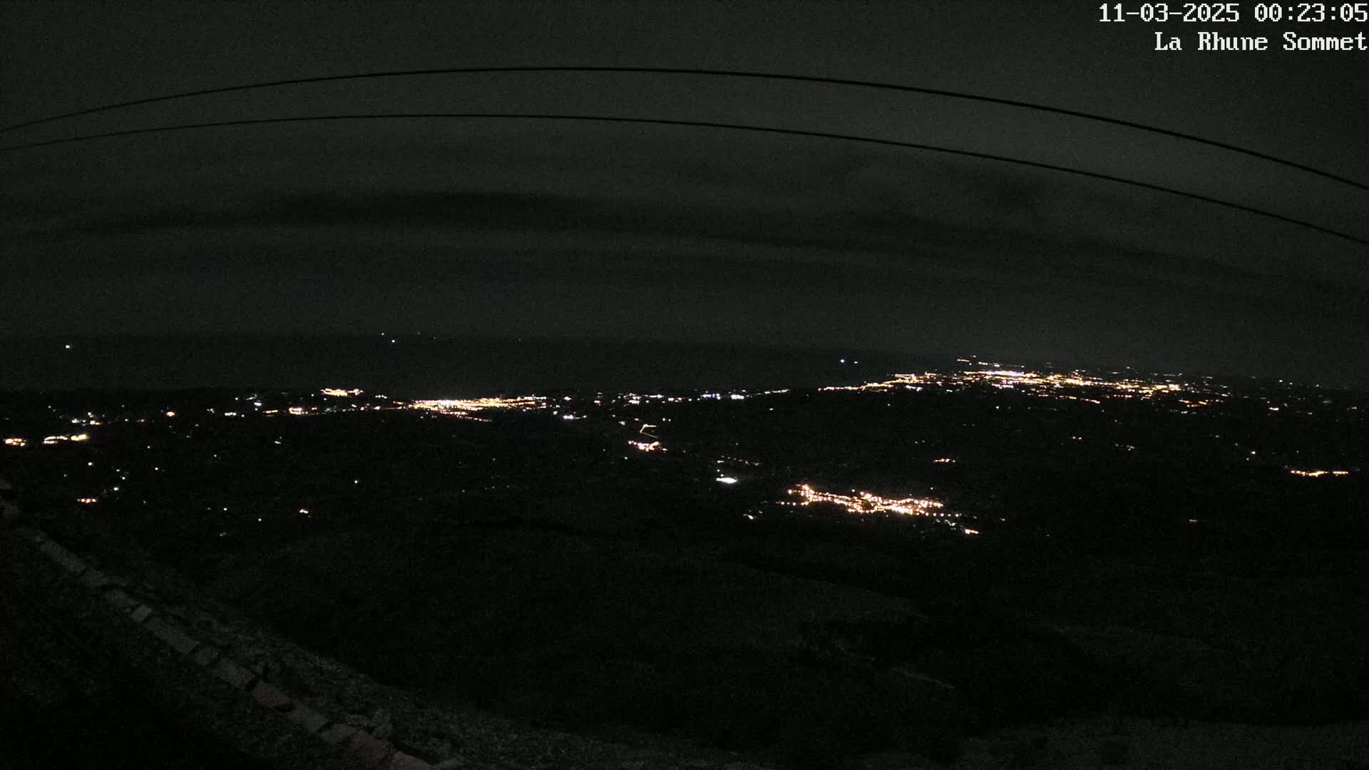 A nighttime, high-angle view shows a sprawling city illuminated by scattered lights extending to a dark horizon under a mostly clear sky.