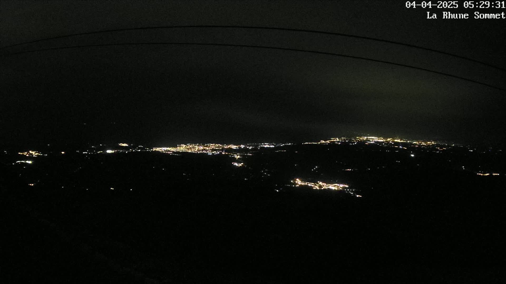 A nighttime view of a distant city illuminated by lights under a dark, cloudy sky.
