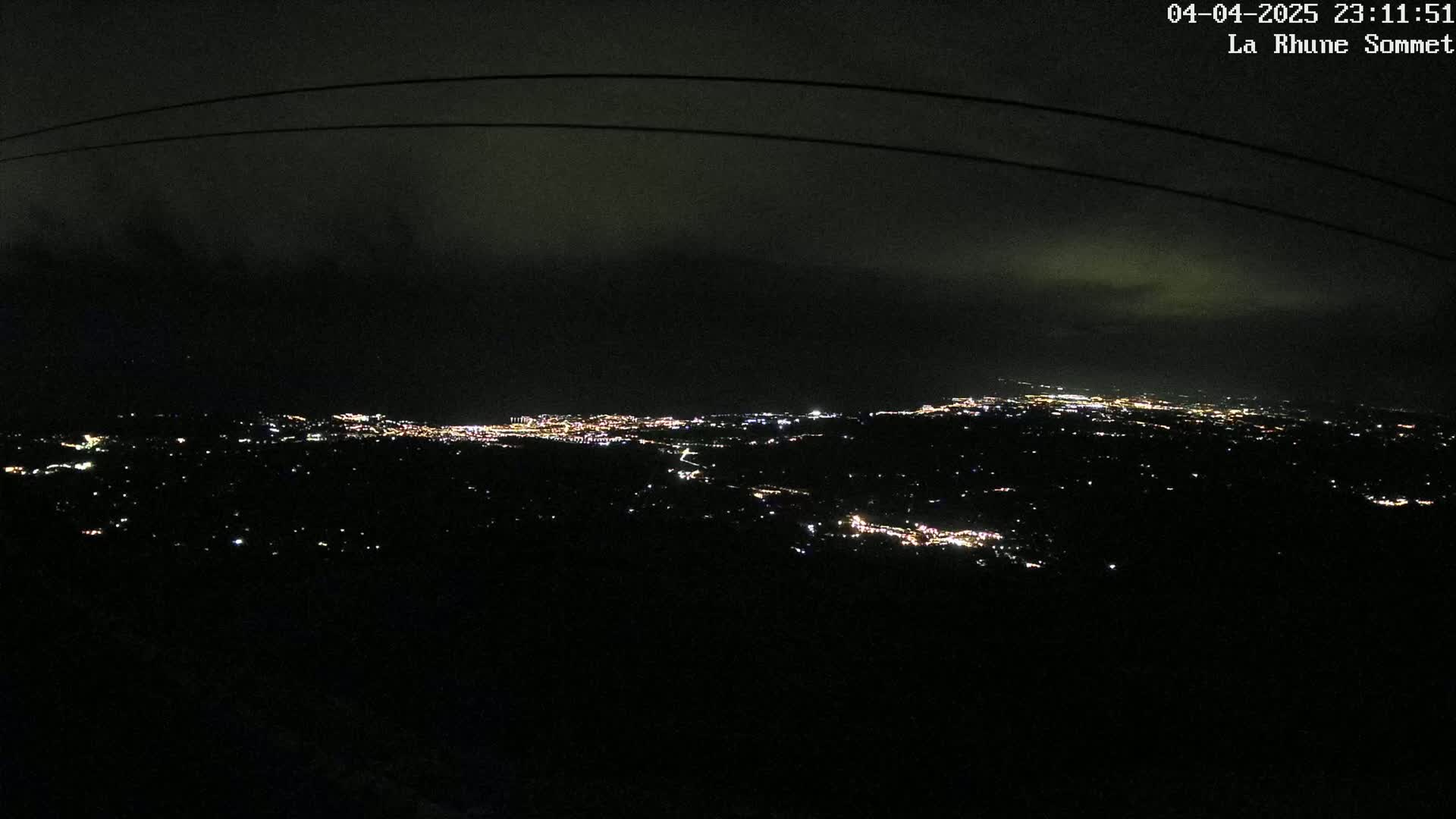 A nighttime, cloudy view of a distant city illuminated by scattered lights, seen from a high vantage point.