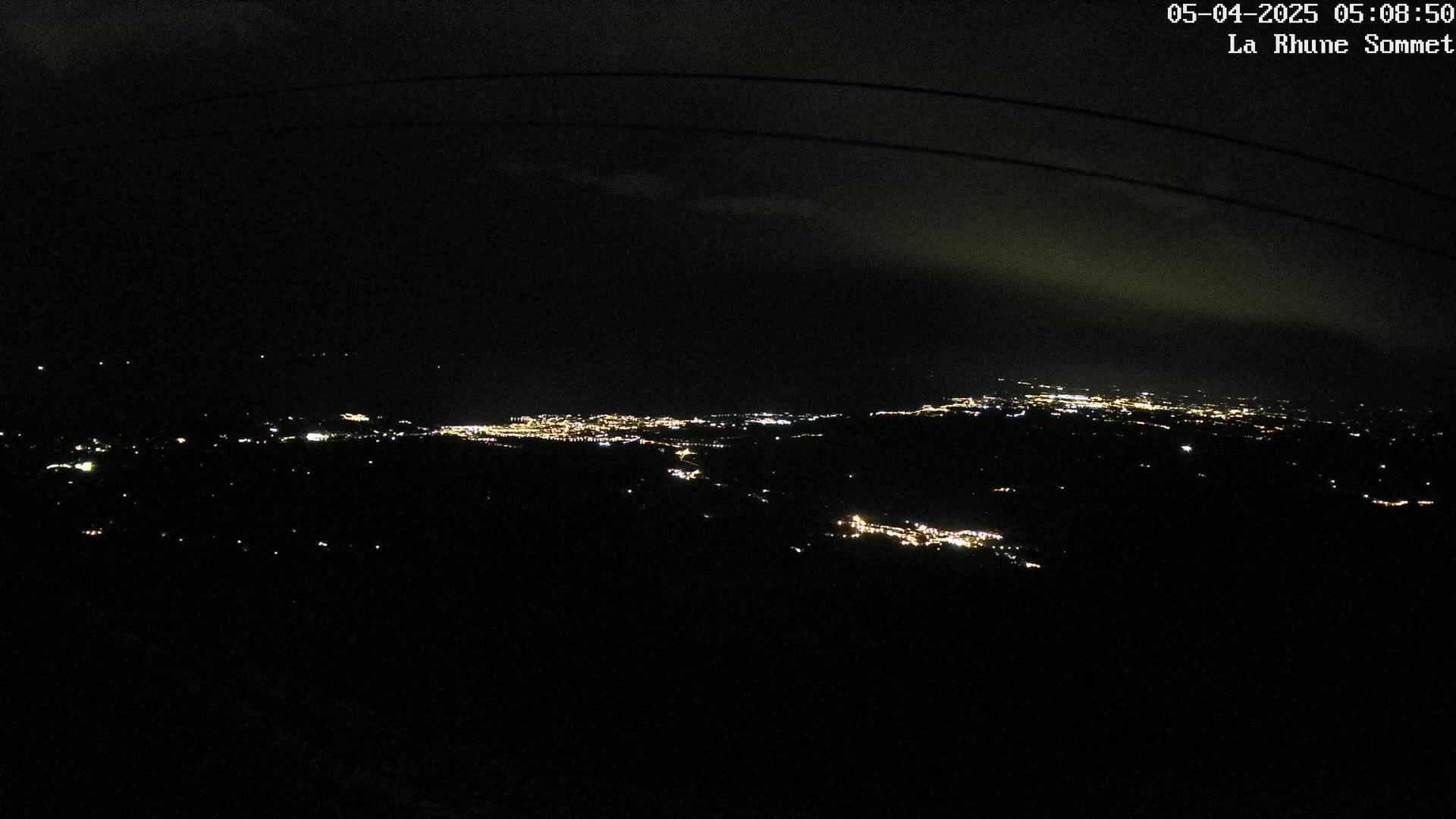 A nighttime, high-angle view shows a distant city illuminated by scattered lights across a dark landscape.