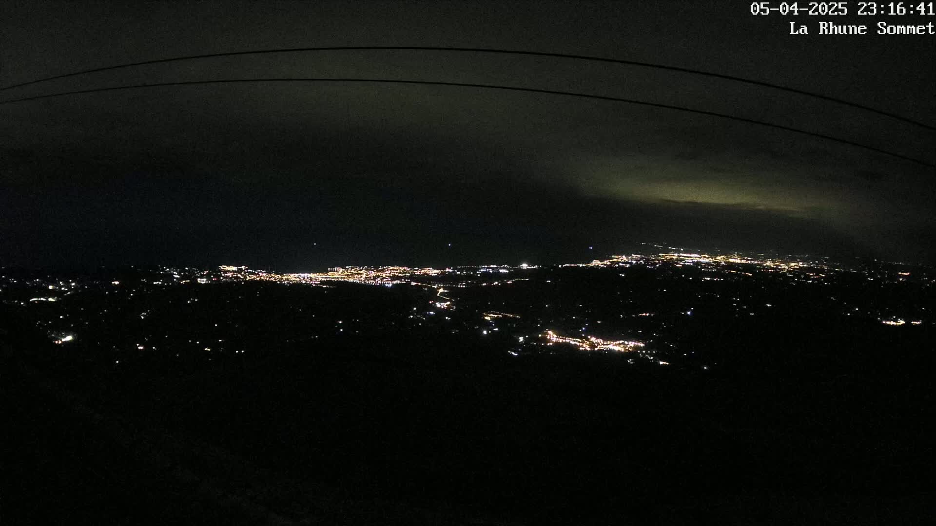A nighttime view of a sprawling city's lights spread across a dark landscape under a mostly cloudy sky.
