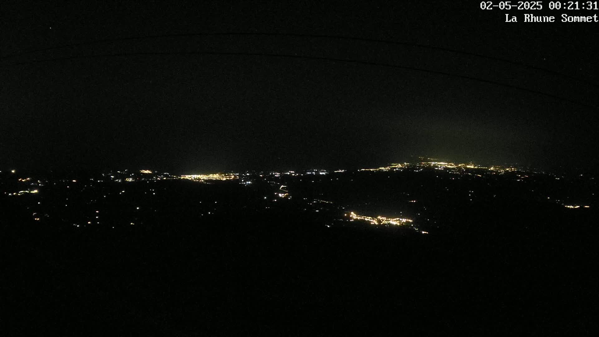 A nighttime view shows a sprawling city illuminated by scattered lights in the distance under a dark sky.
