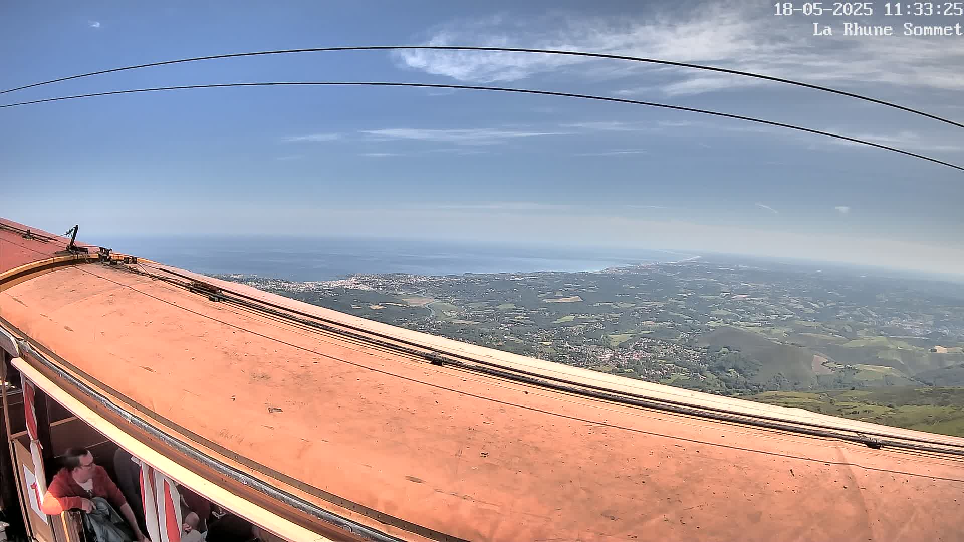 A cable car ascends, revealing a panoramic view of a coastline and sprawling landscape under a clear, sunny sky.