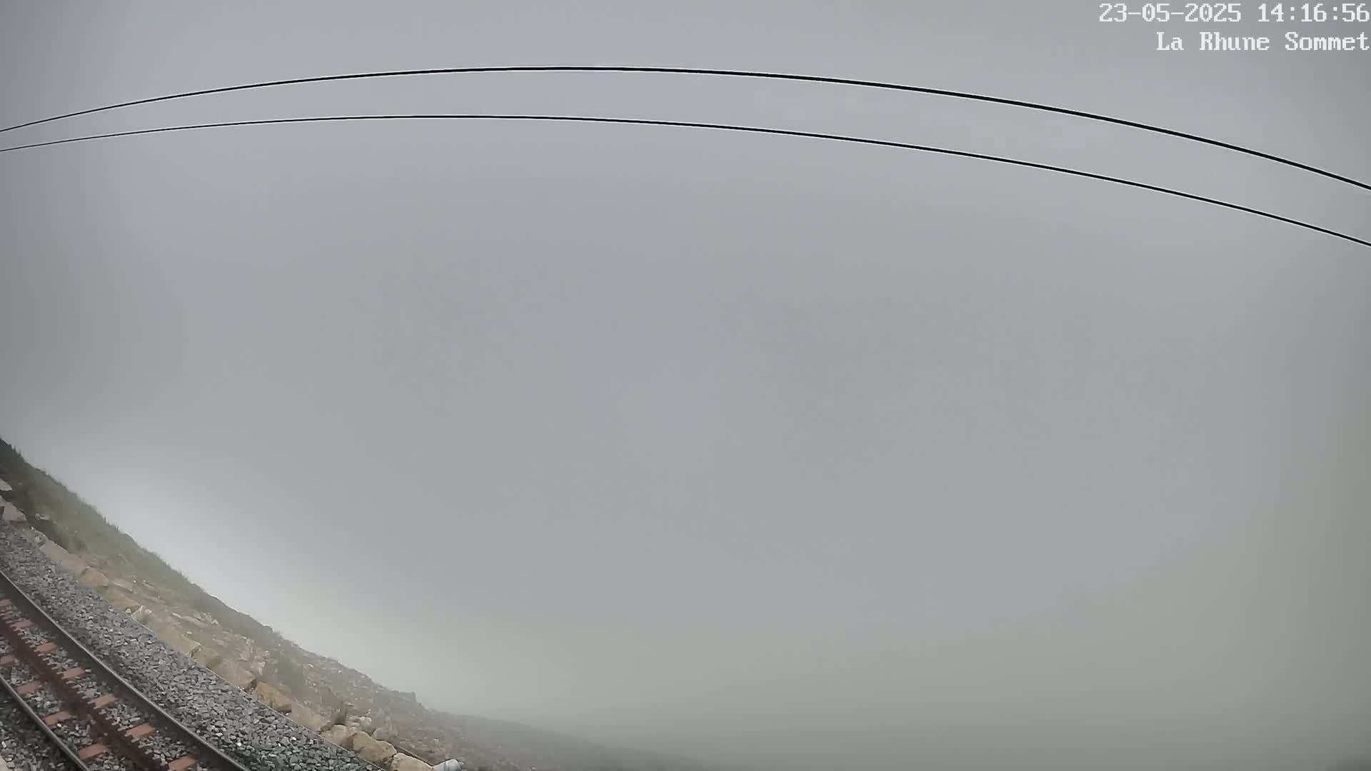 A train track curves alongside a rocky hillside shrouded in thick fog.