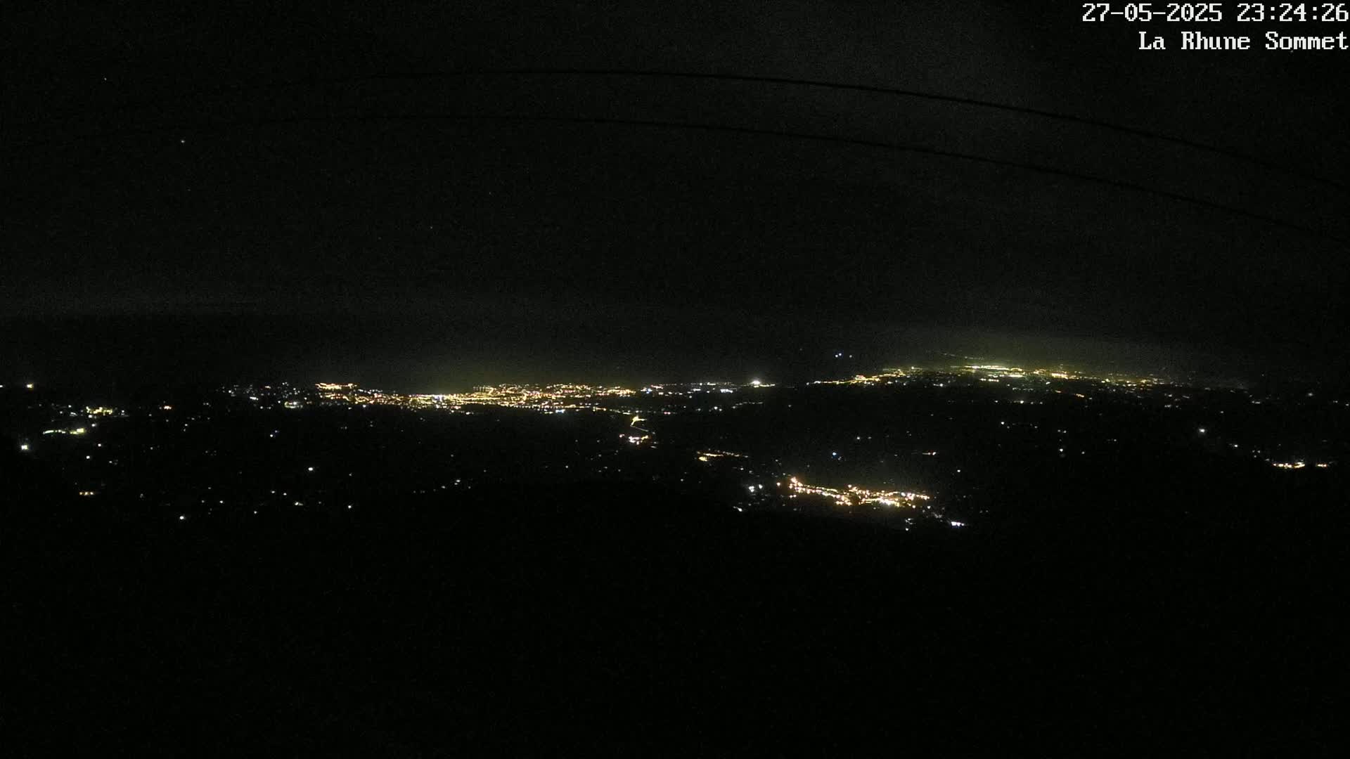 A nighttime, high-angle view shows a sprawling city illuminated by scattered lights against a dark sky.