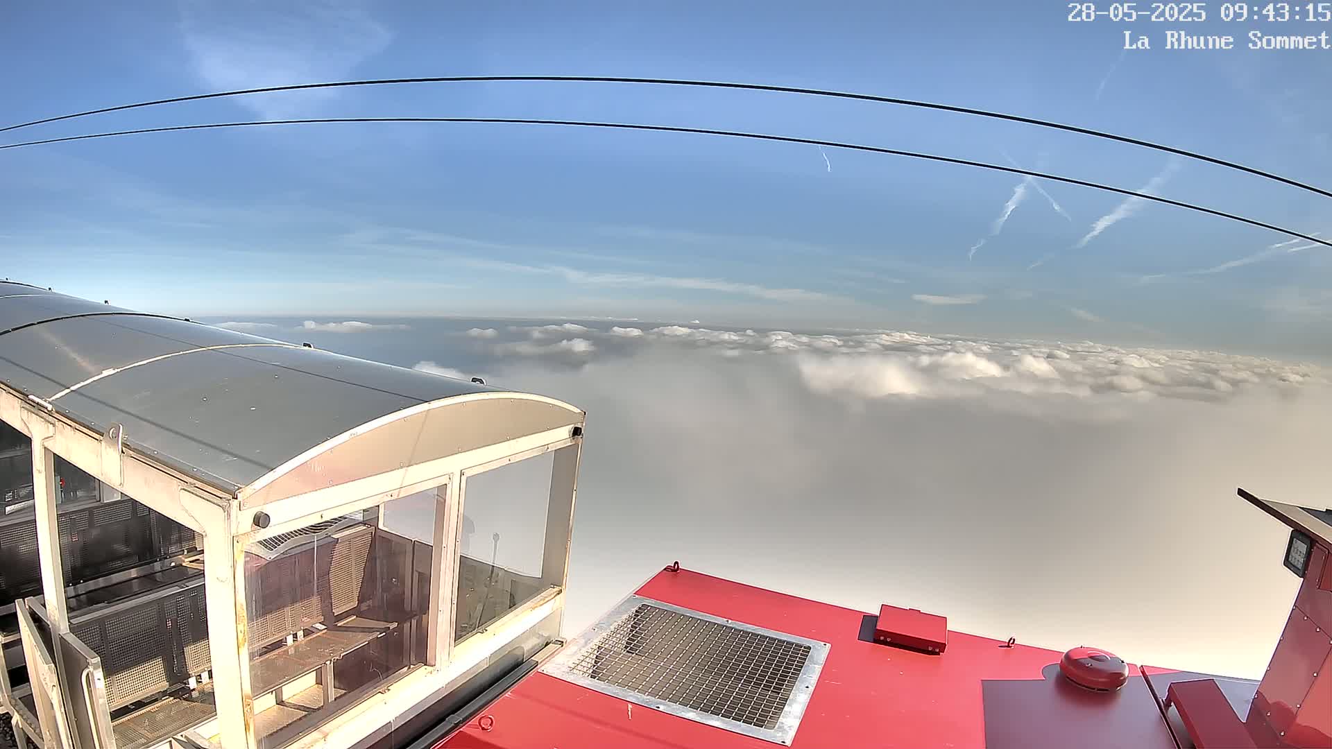 A cable car with a mostly glass enclosure is positioned above a vast expanse of clouds under a clear blue sky.