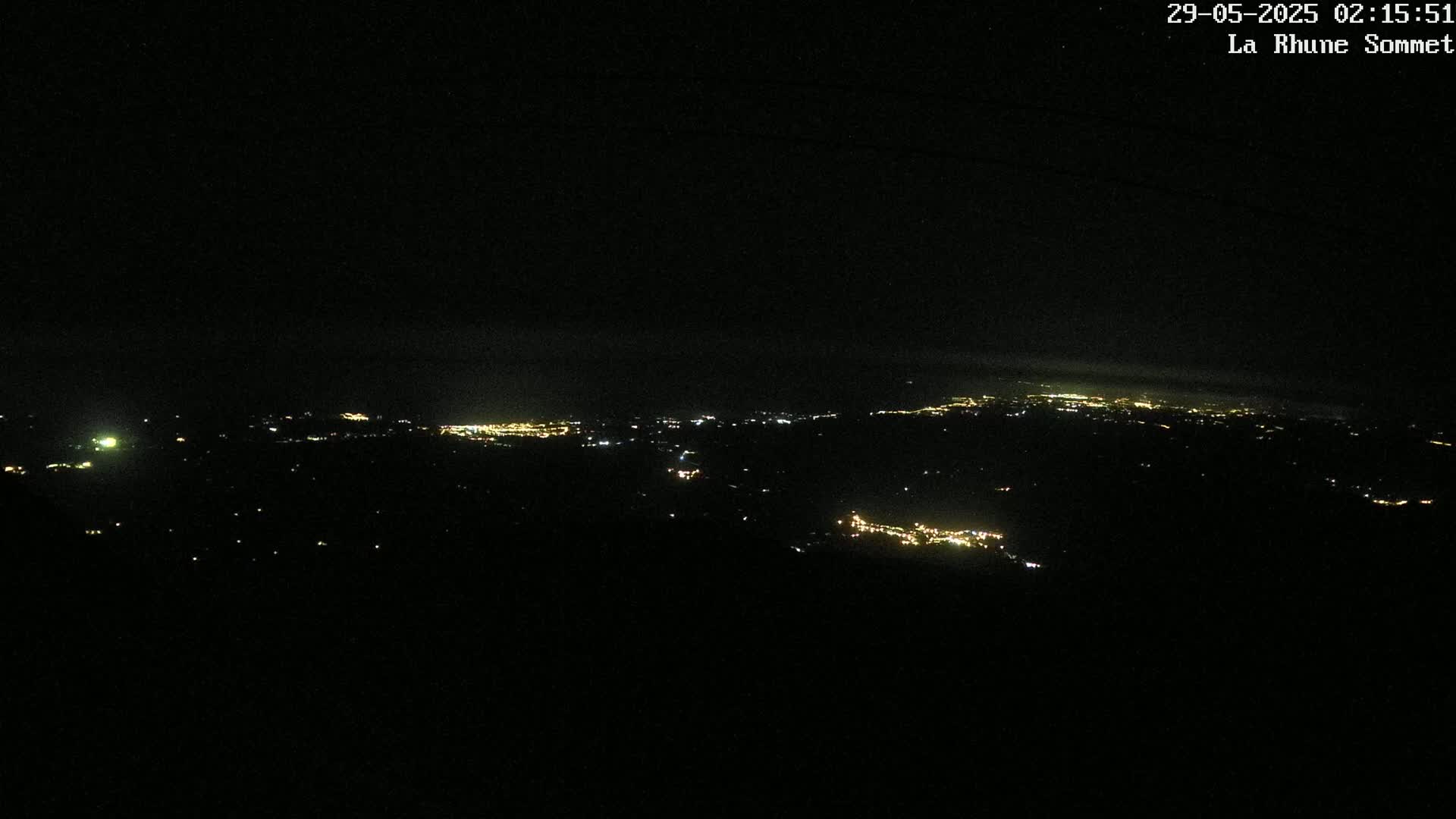 A nighttime view from a high vantage point shows a distant expanse of scattered city lights under a dark, clear sky.