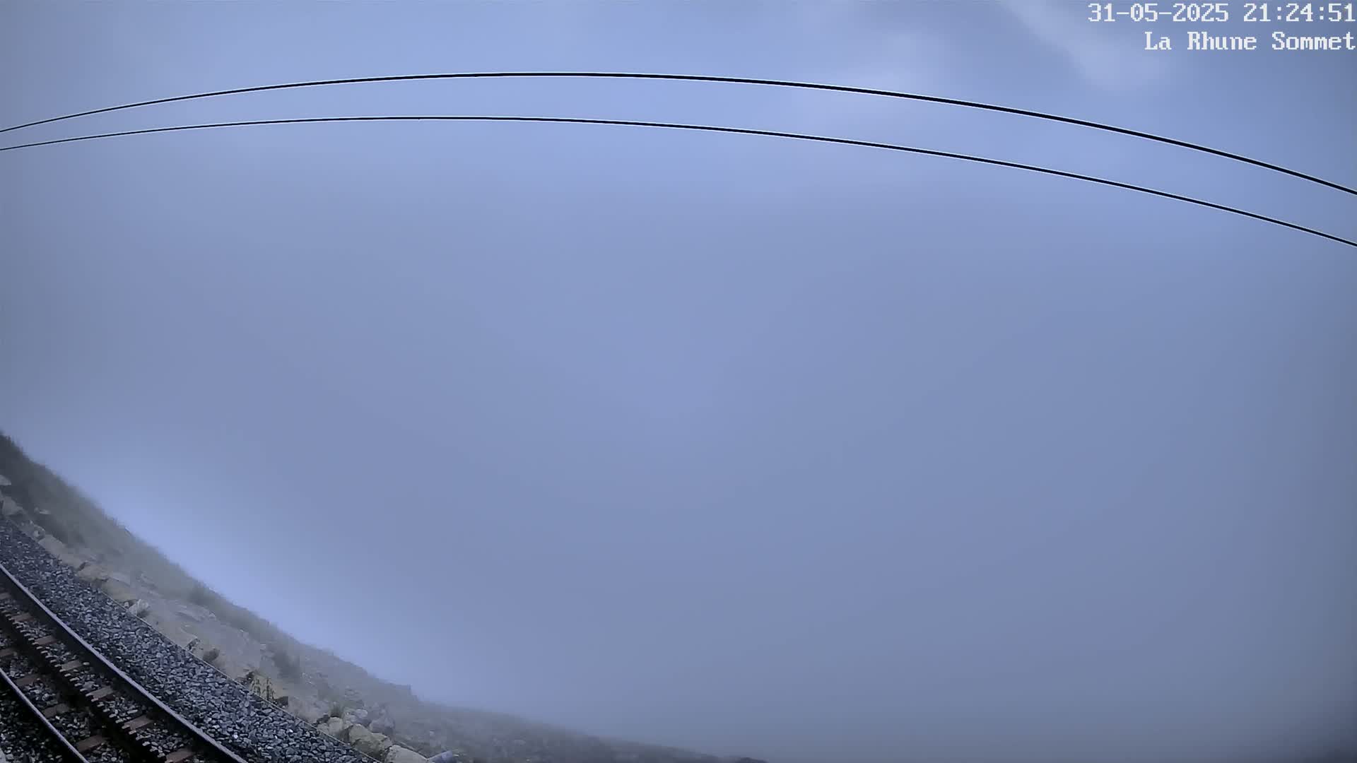 A train track runs alongside a rocky hillside shrouded in thick fog under a gray sky.