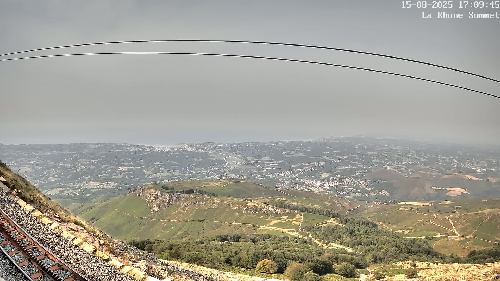 A railway track runs alongside a rocky hillside shrouded in thick fog, with power lines arching overhead.