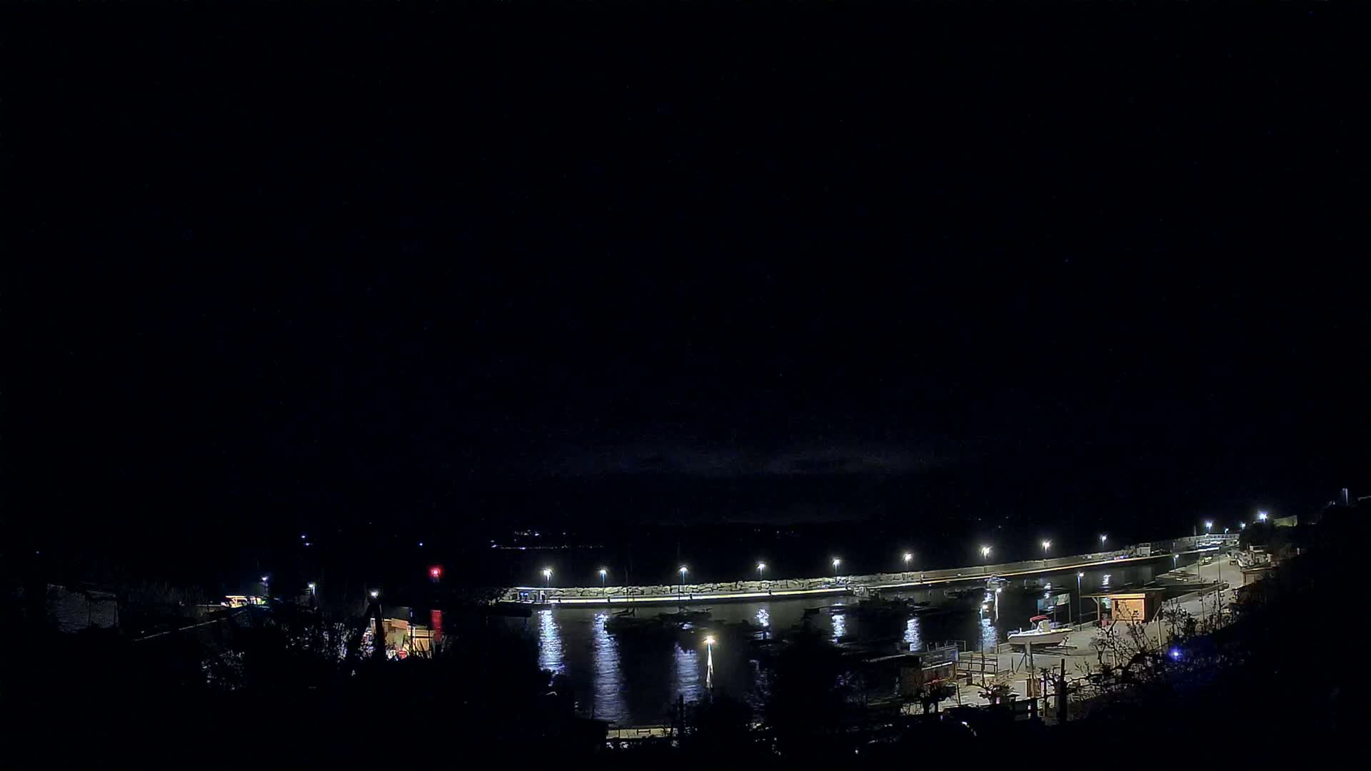 A nighttime view of a harbor with boats moored along a lit pier under a dark sky.