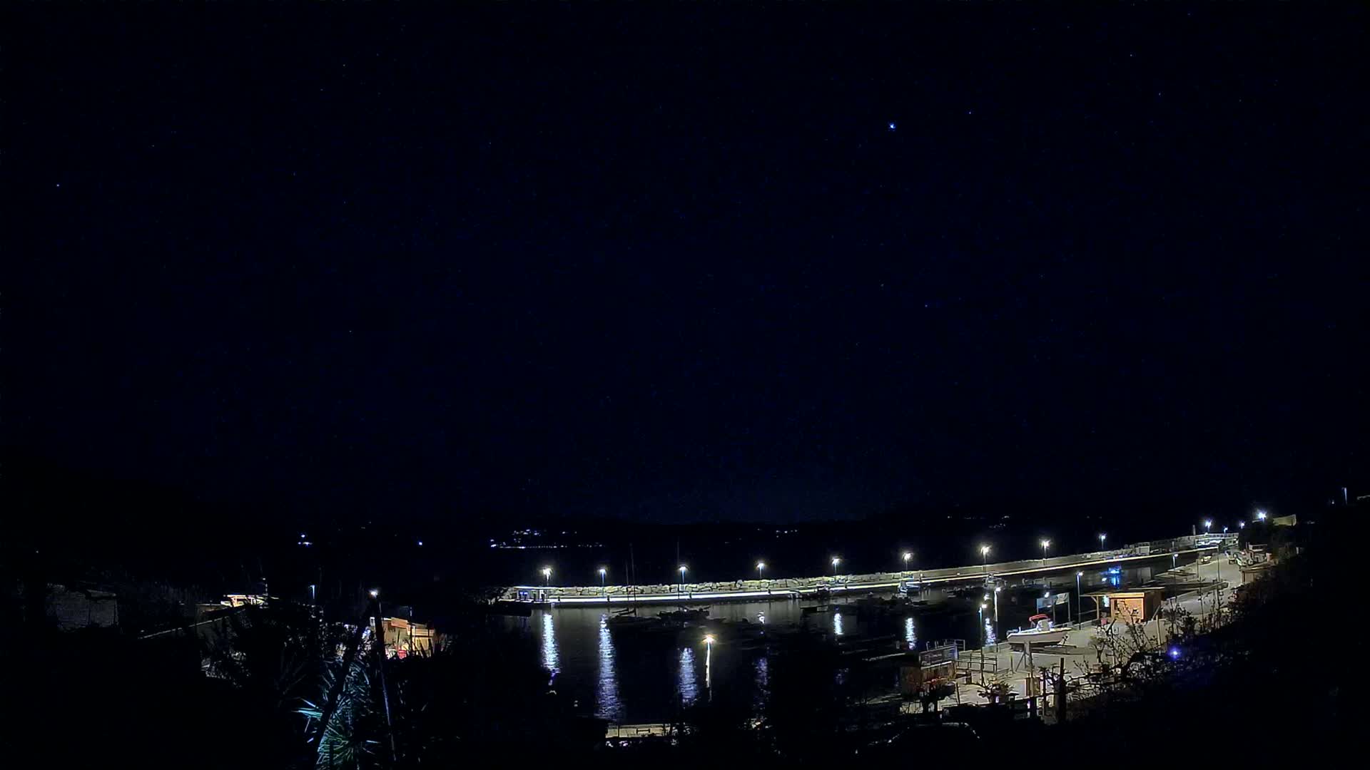 A nighttime view of a harbor filled with boats under a clear, starry sky.