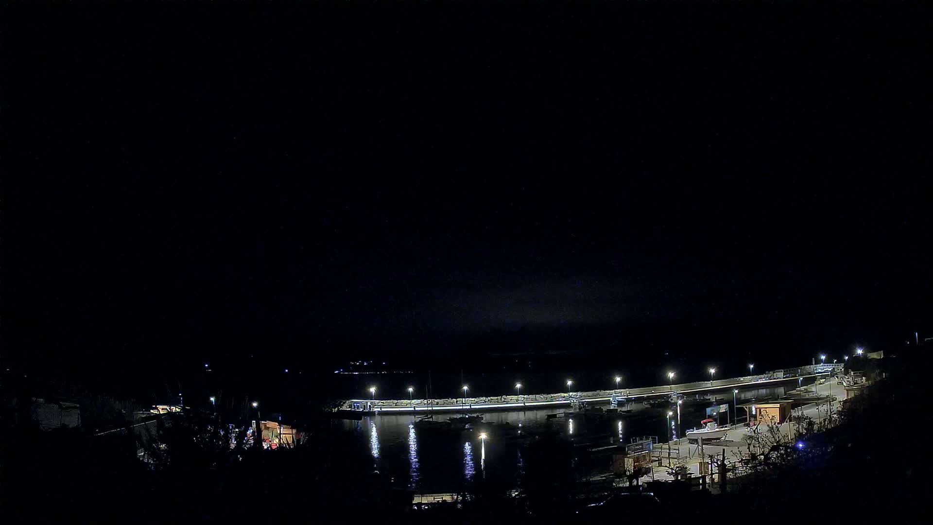 A nighttime view of a harbor with boats docked along a lit pier under a dark, clear sky.