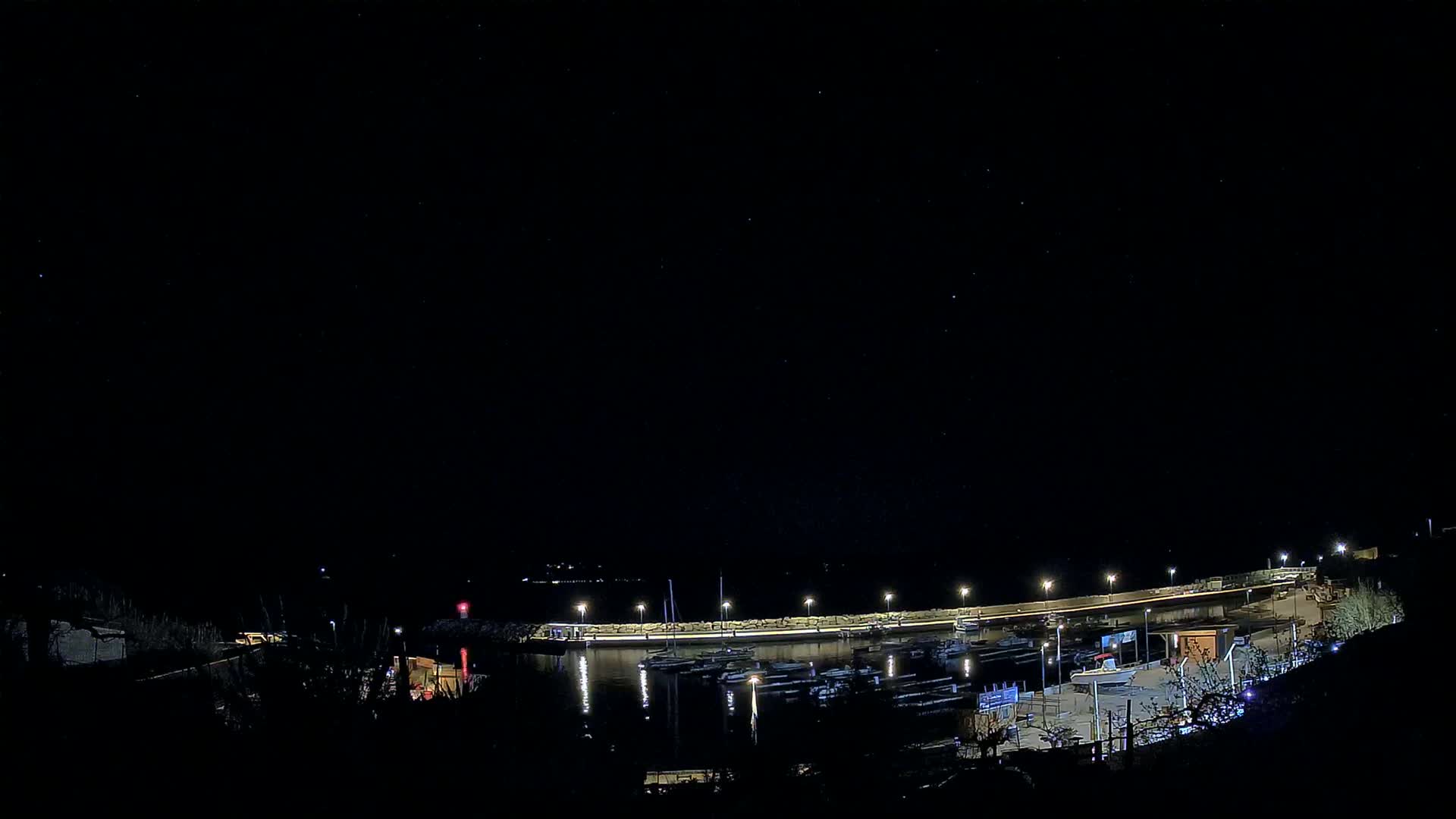 A nighttime view of a harbor filled with boats under a clear, starry sky.