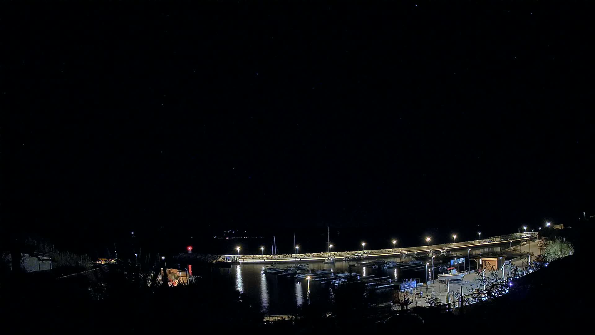 A small, illuminated harbor filled with boats is visible under a clear, starry night sky.