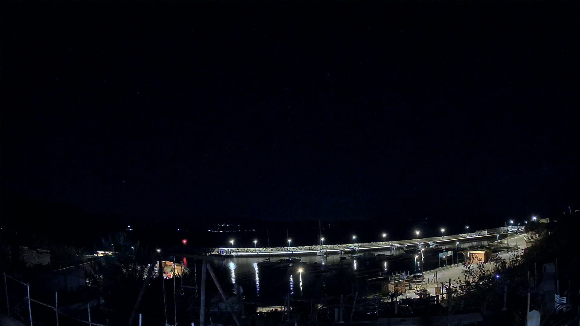 A nighttime view of a harbor with boats and illuminated docks under a clear, starry sky.