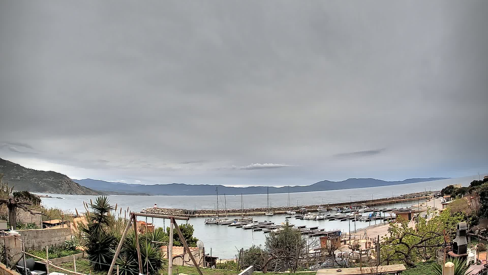 A small marina filled with boats is nestled between hills under a heavily overcast sky.