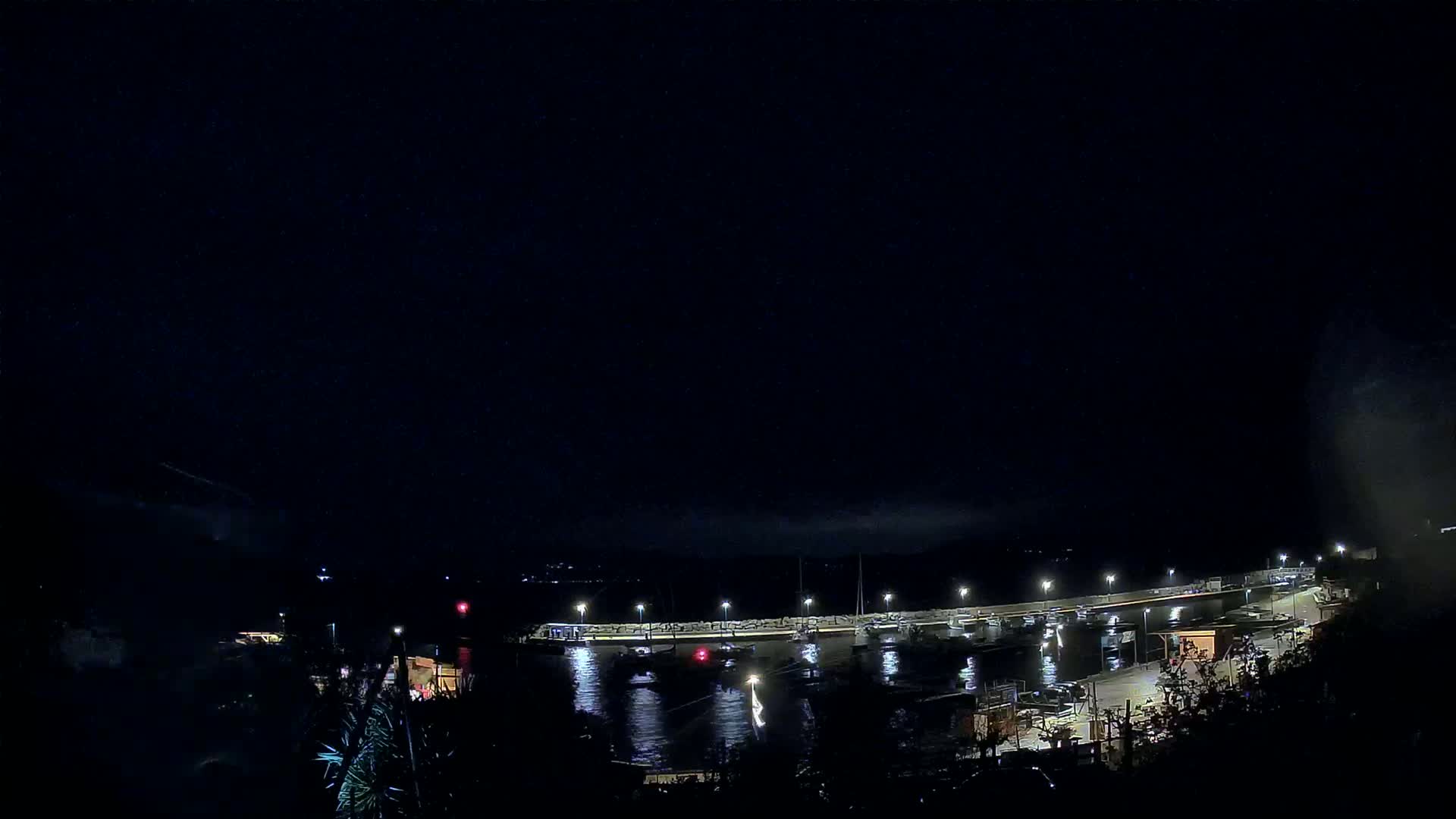 A nighttime view of a harbor with boats docked along a lit pier under a dark, clear sky.