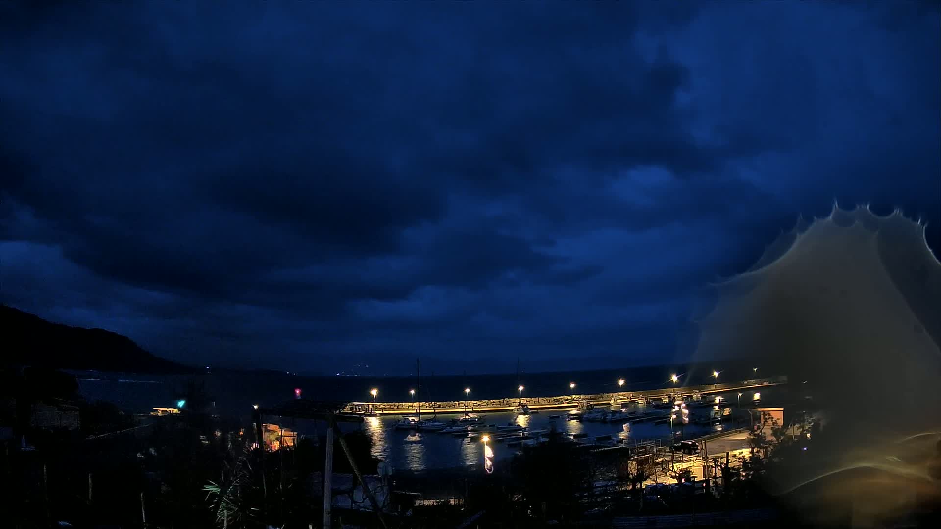 A nighttime view of a harbor filled with boats under a dark, cloudy sky.