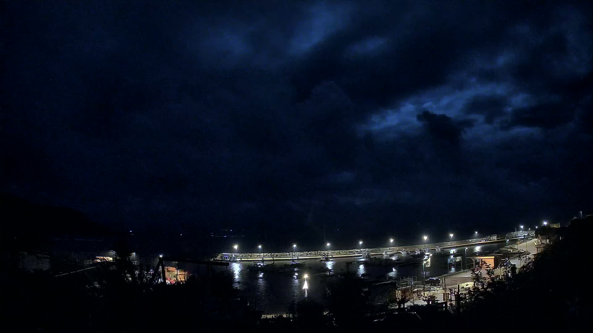 A nighttime view of a harbor filled with boats under a dark, cloudy sky.