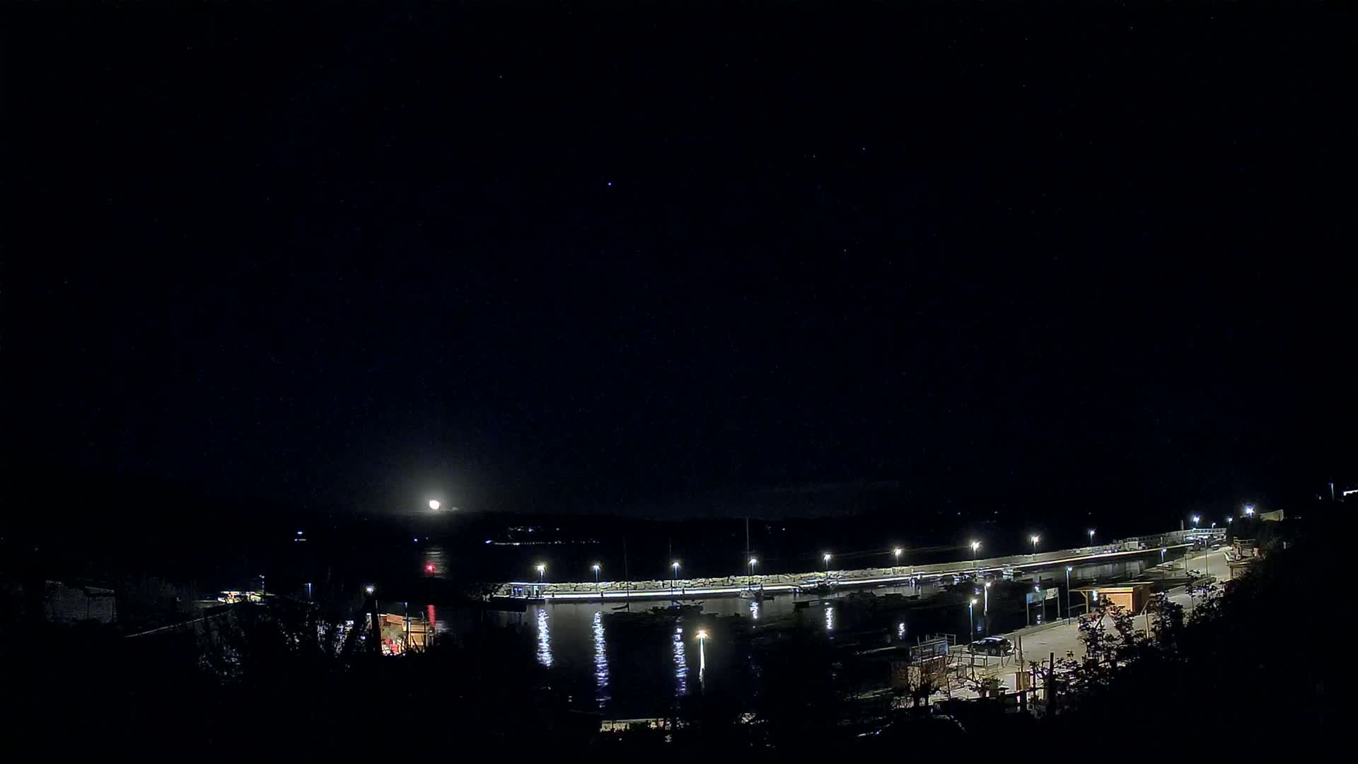 A moonlit night scene shows a harbor with boats moored along a lit pier.