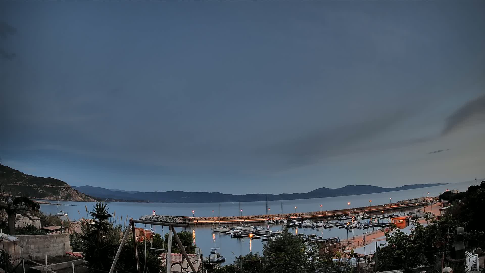A small harbor filled with boats is nestled between hills under a dusky, overcast sky.
