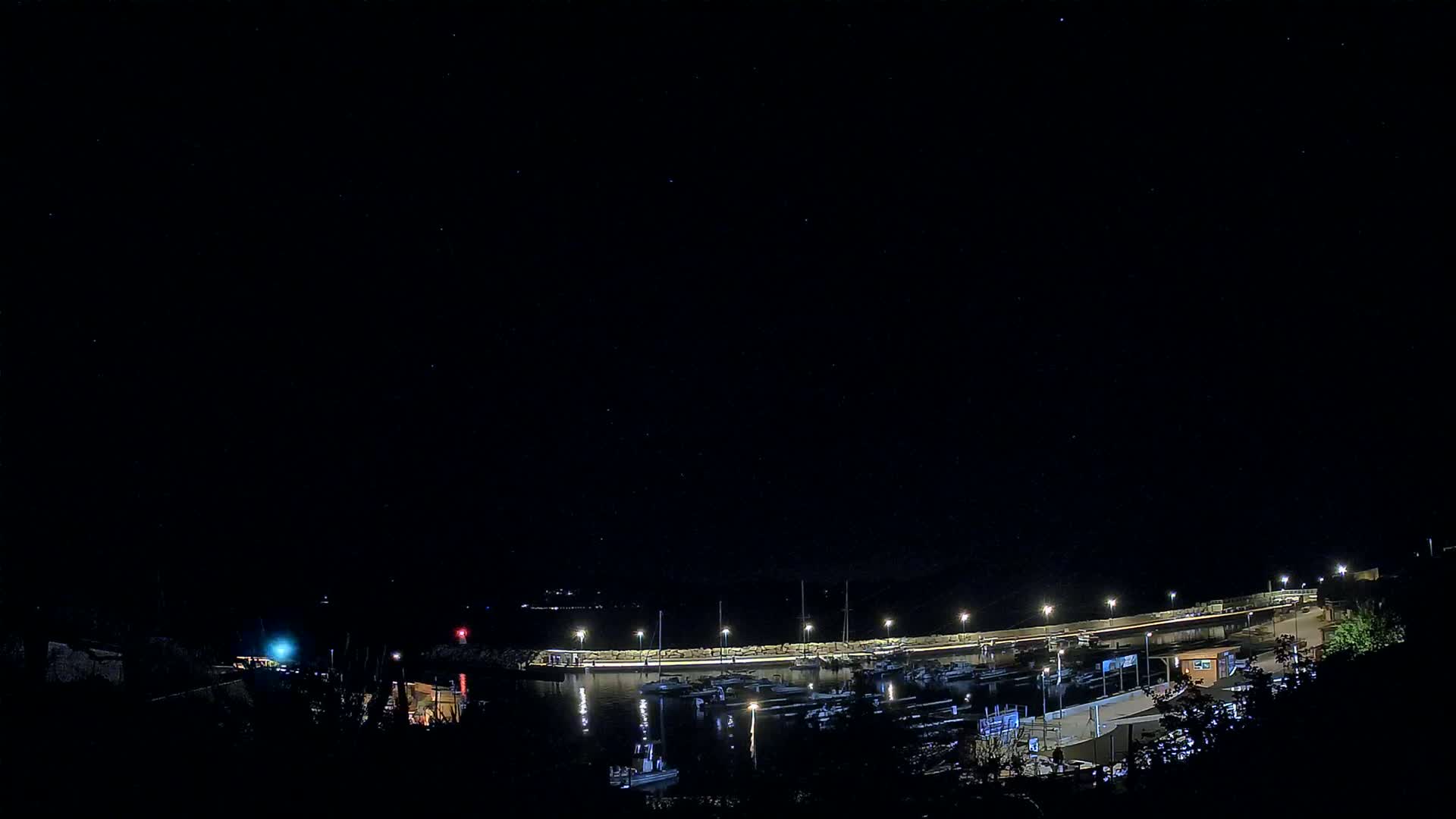 A nighttime view of a harbor filled with boats under a clear, starry sky.