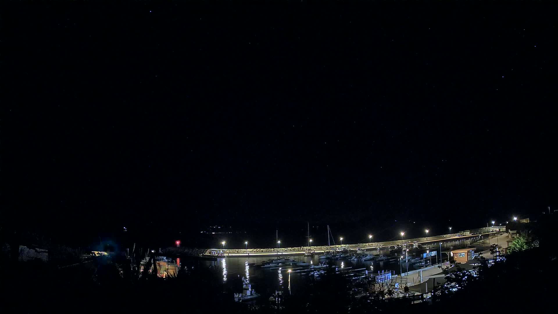 A nighttime view of a harbor filled with boats under a clear, starry sky.