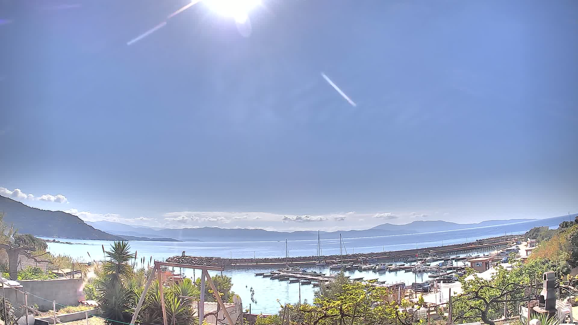 A sunny day reveals a calm bay filled with boats, a small town nestled beside it, and mountains in the distance.
