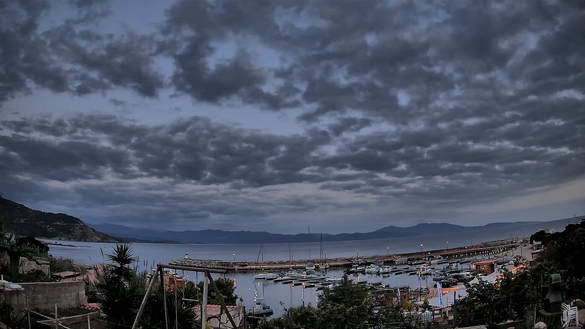 A harbor filled with boats is nestled between hills under a cloudy, overcast sky.