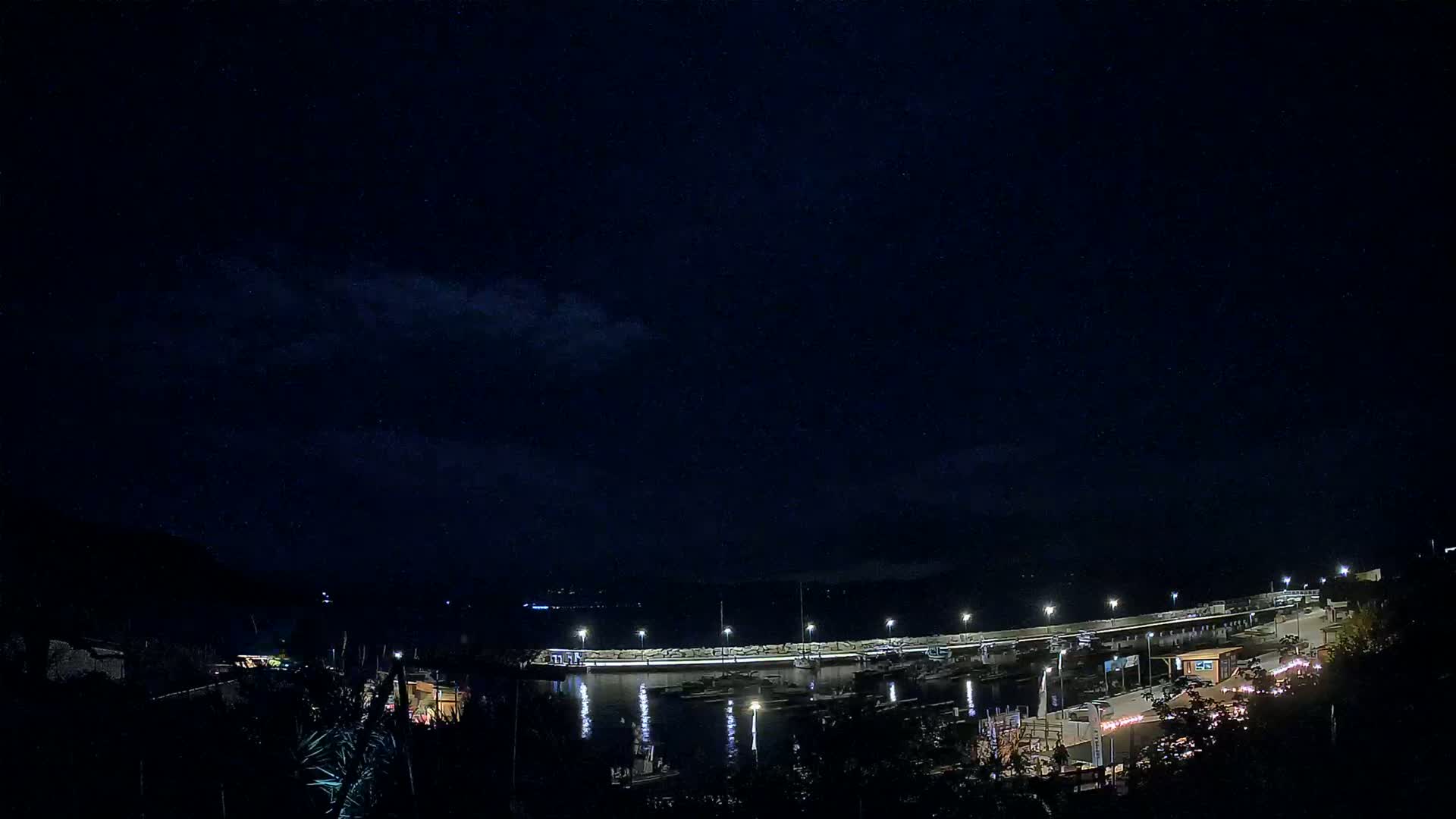 A nighttime view of a harbor with boats docked under a mostly clear, dark sky.