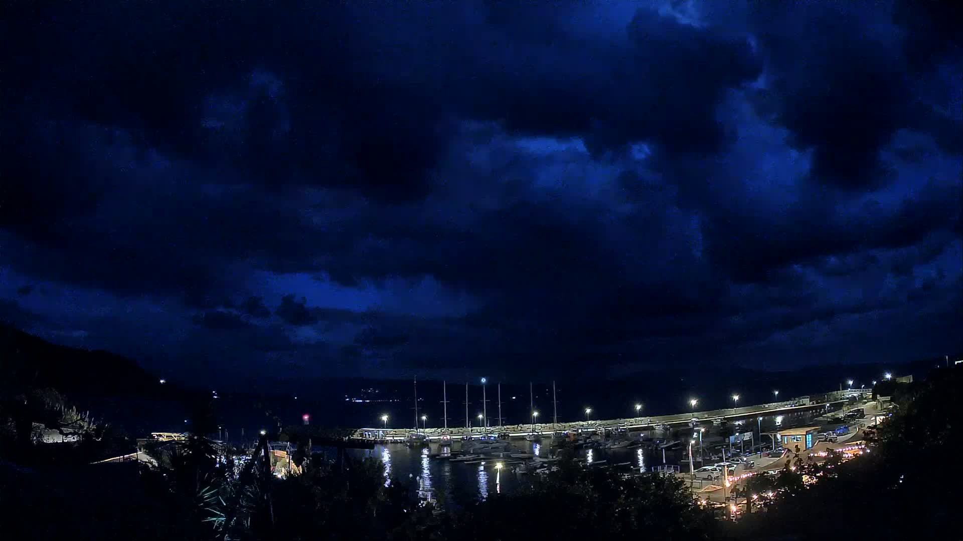 A nighttime view of a marina filled with boats under a dark, cloudy sky.
