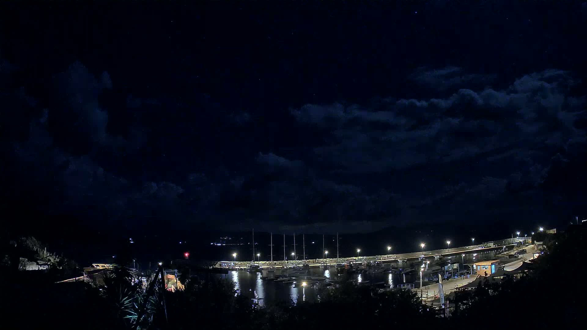 A nighttime view of a marina filled with boats under a partly cloudy sky.