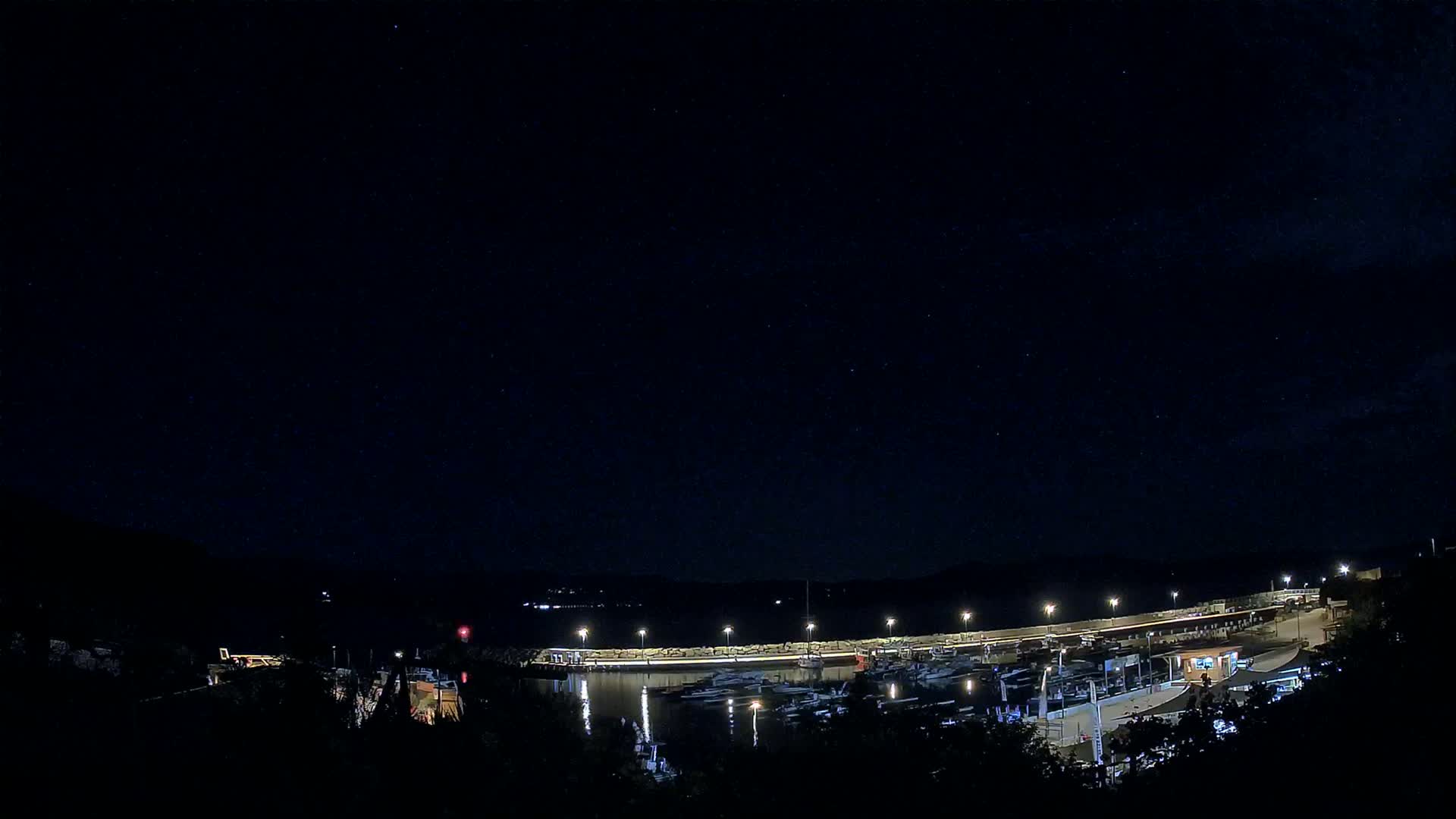 A nighttime view of a marina filled with boats under a clear, starry sky.