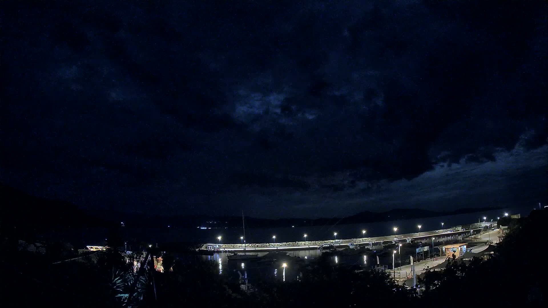 A nighttime view of a harbor with boats docked under a dark, cloudy sky.