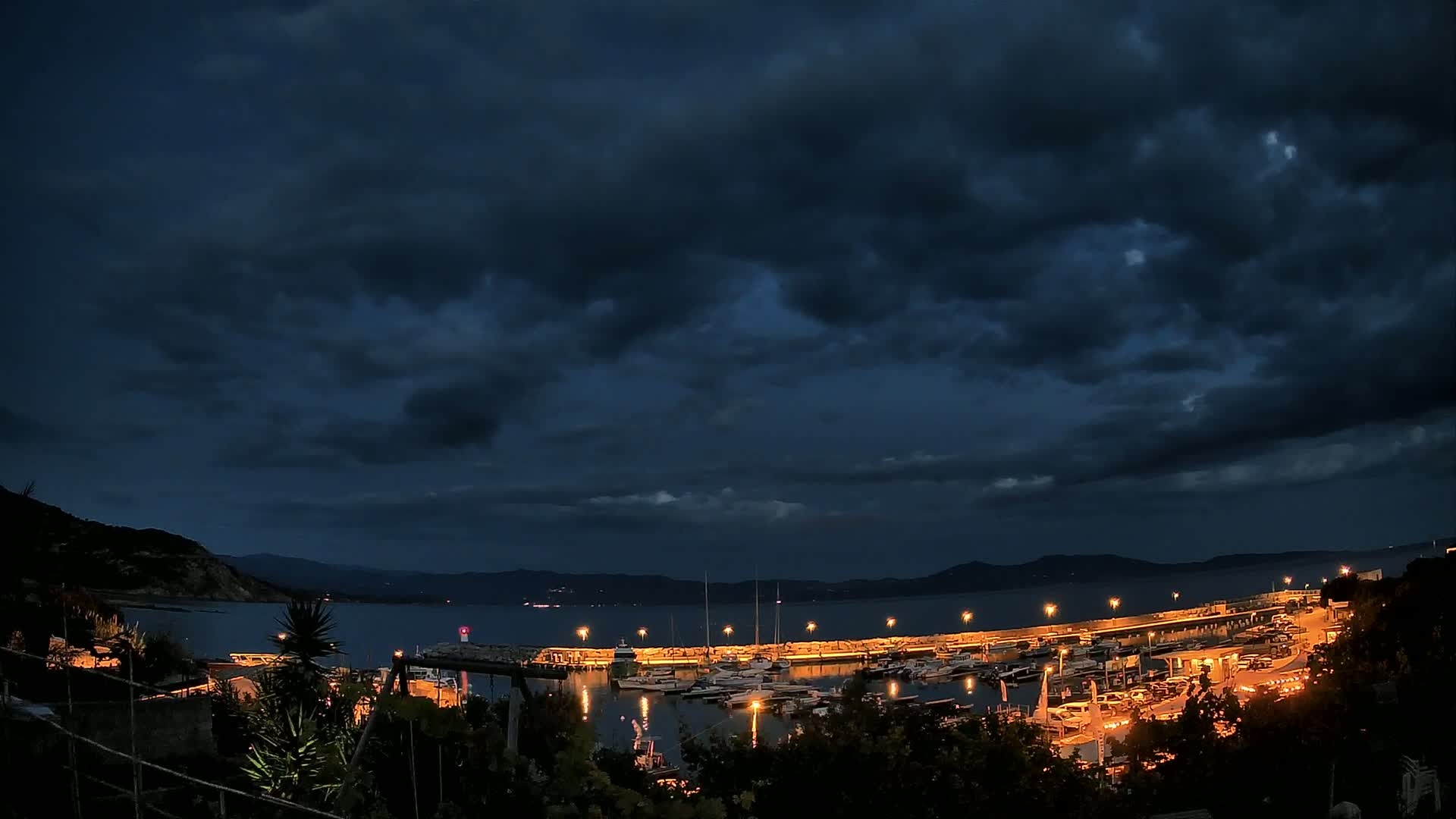 A nighttime view of a harbor filled with boats under a dark, cloudy sky.