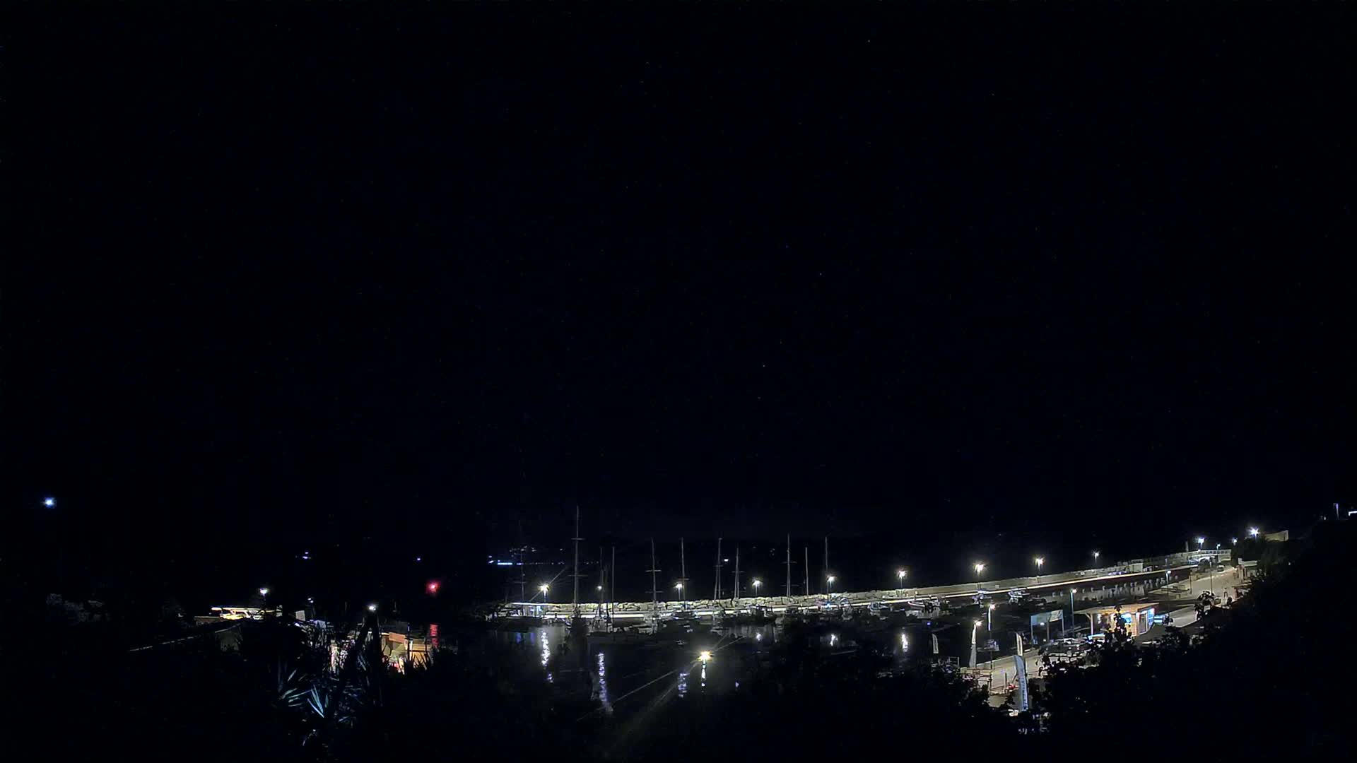 A marina filled with boats is illuminated at night under a clear, dark sky.