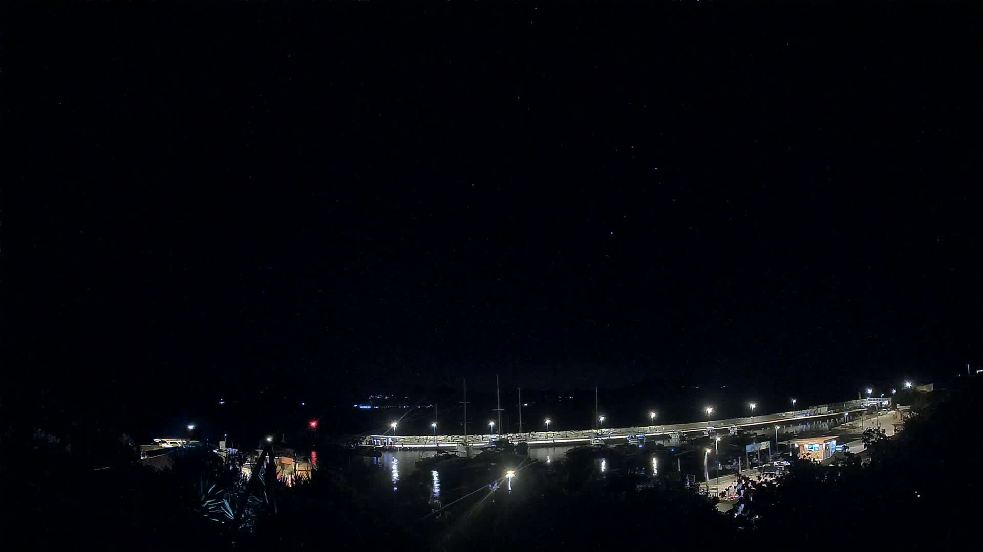 A nighttime view of a harbor with boats docked under a clear, starry sky.